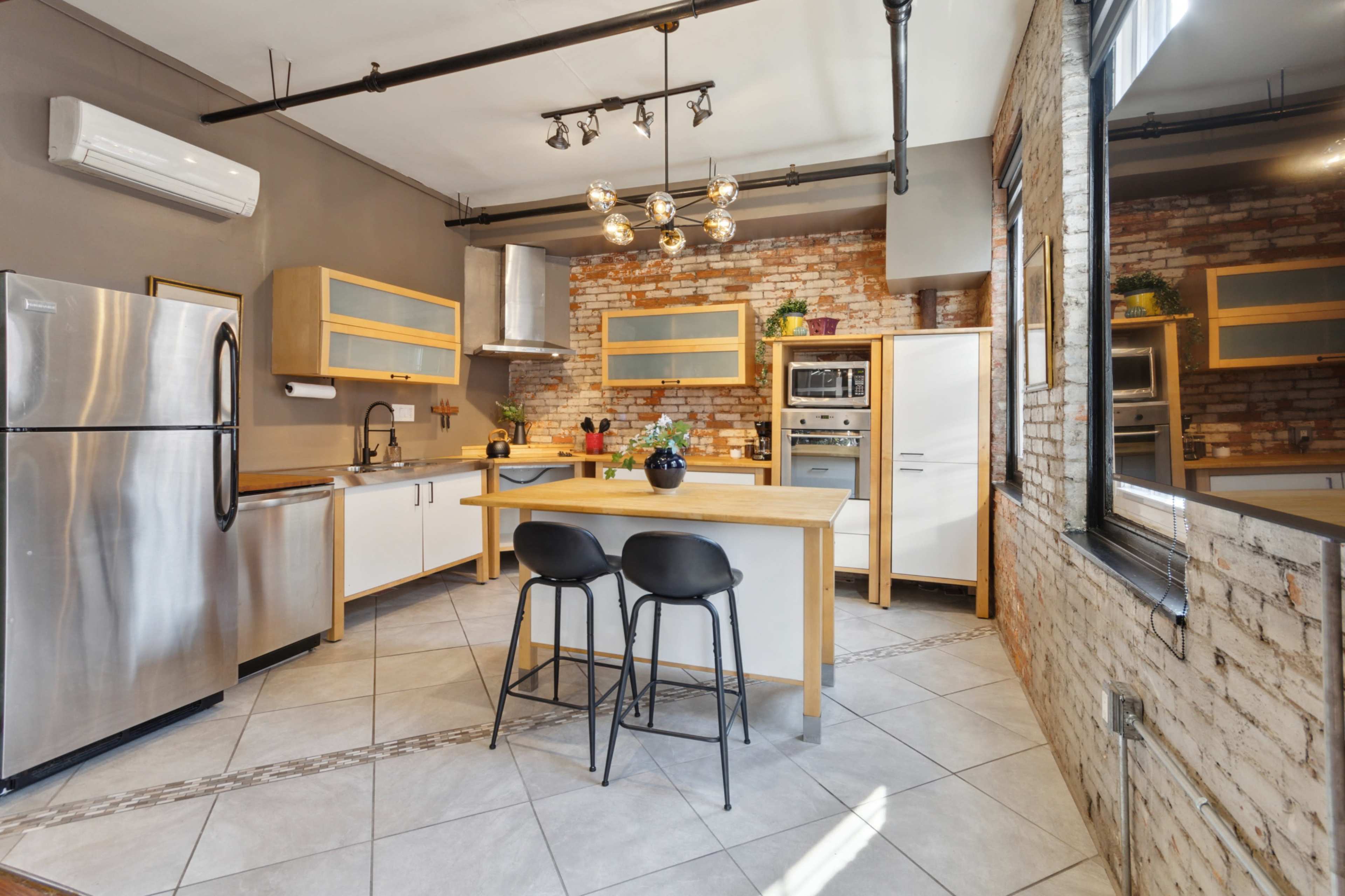 A modern kitchen with stainless steel appliances, wooden cabinetry, and a central island with two black stools.