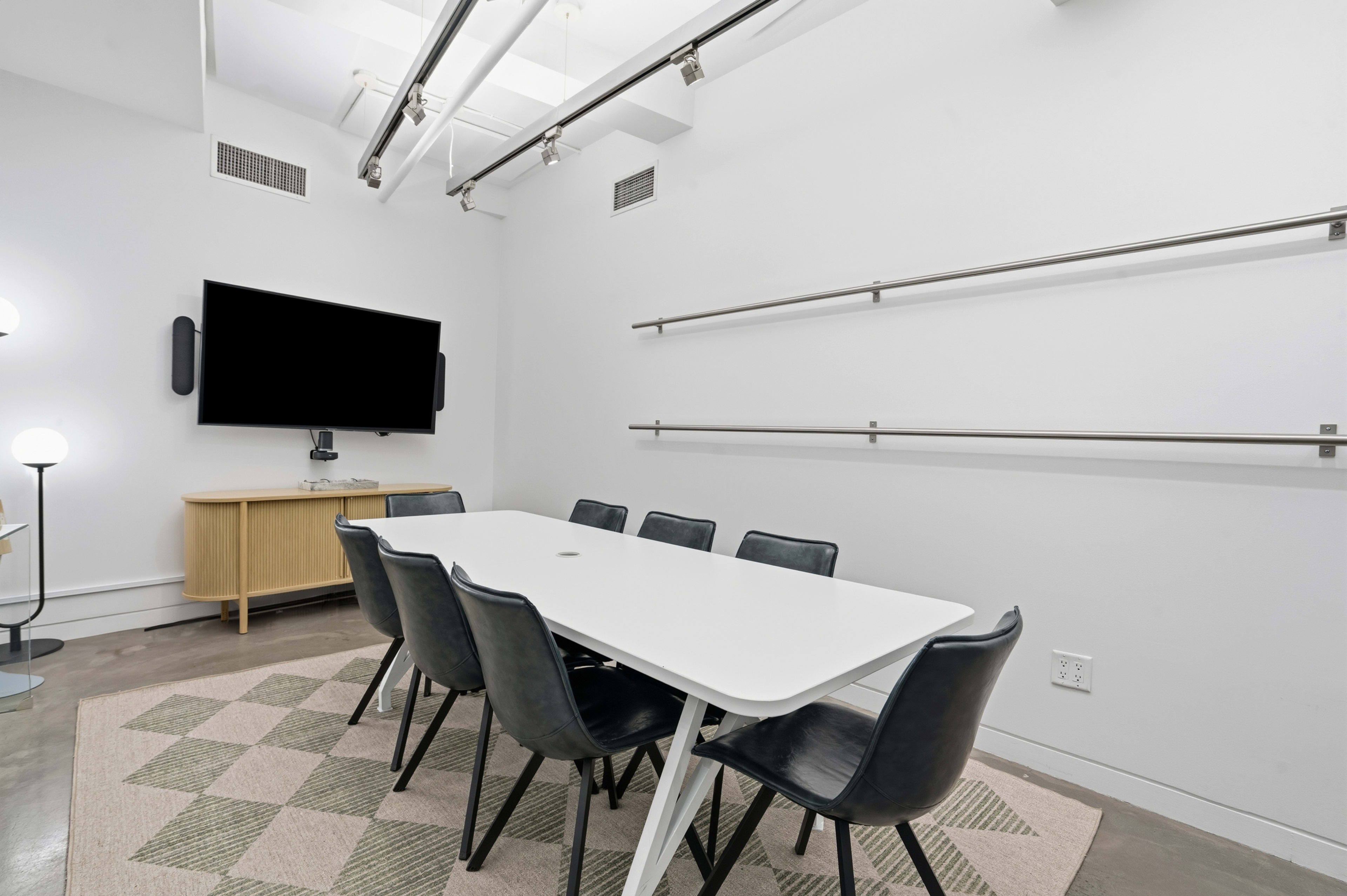 A modern conference room features a white table, black chairs, a wall-mounted television, and minimalist decor.
