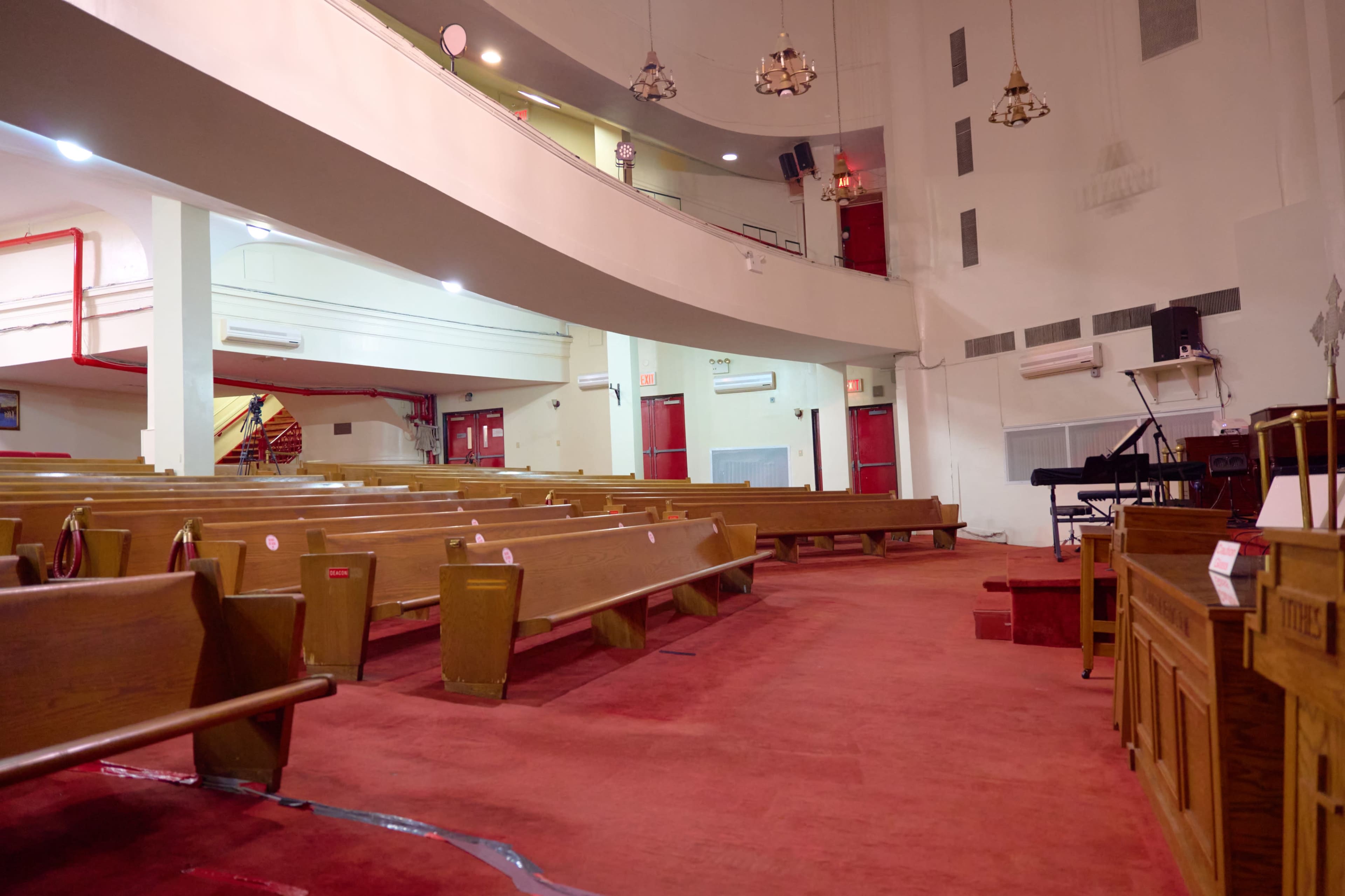 The interior of a church features rows of wooden pews, a carpeted floor, and a raised platform with a musical instrument and a pulpit.