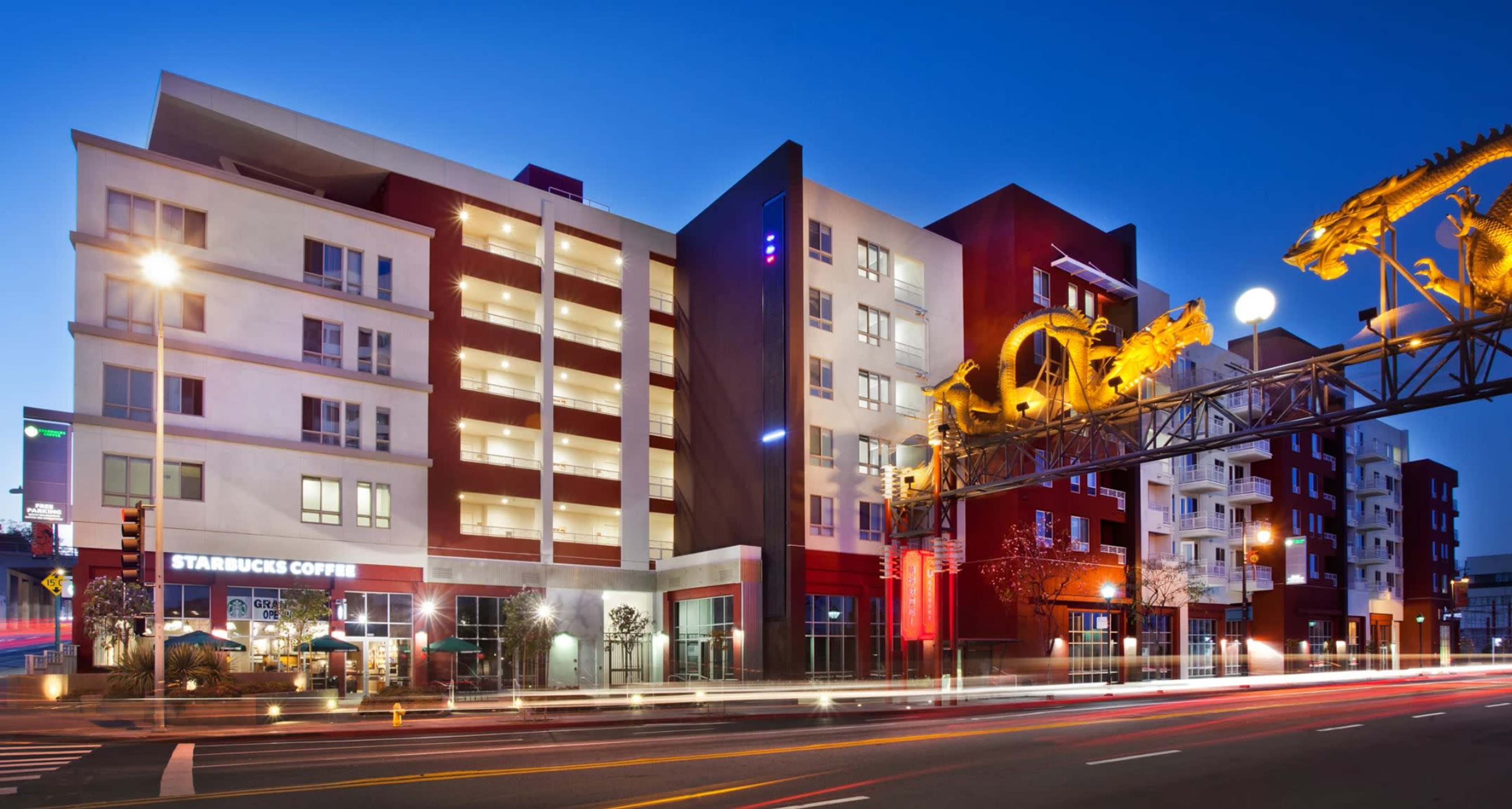 The image features a modern multi-story building with a Starbucks on the ground floor and a prominent decorative structure above it, illuminated at night.