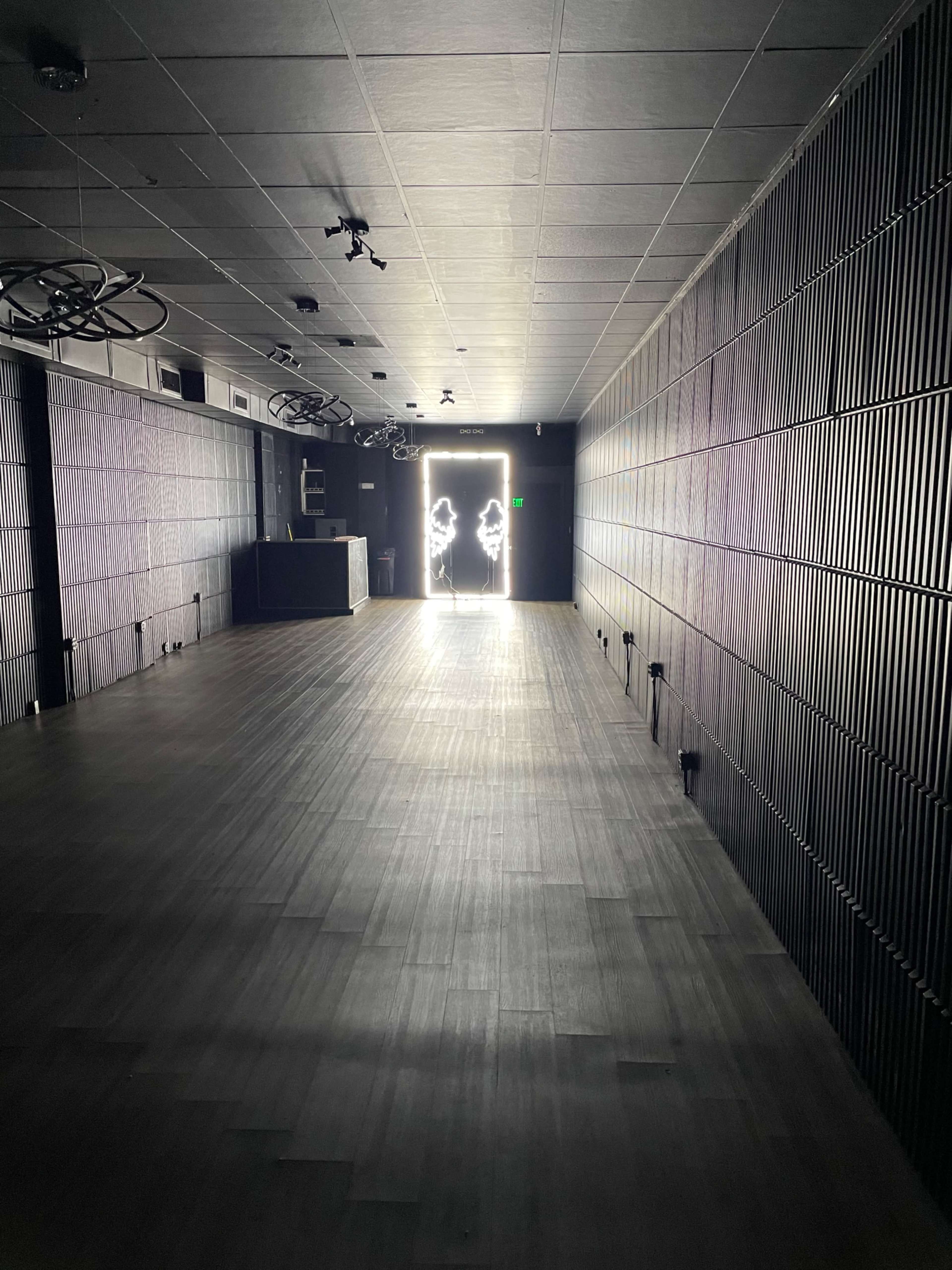 A dimly lit room features a door at the far end, with silhouettes visible in the light streaming through.