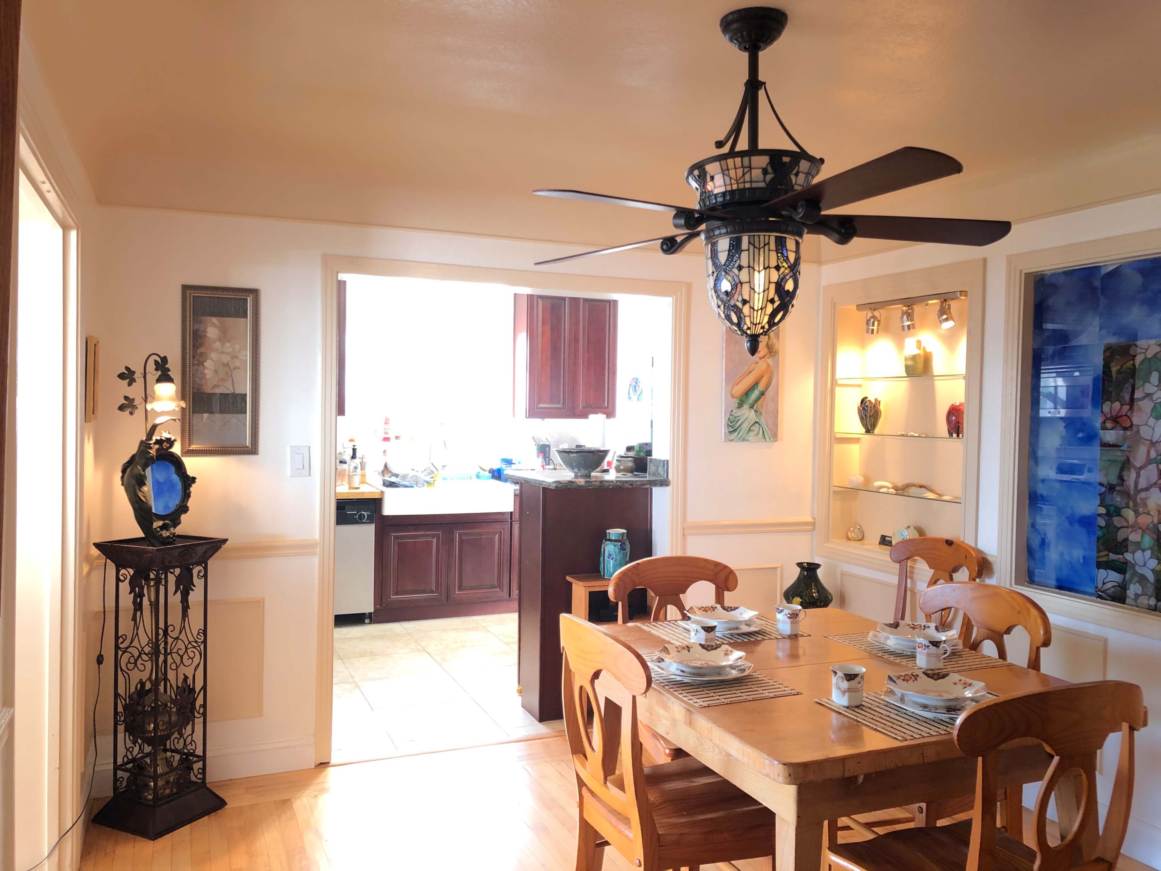 A dining area features a wooden table set with dishes and a ceiling fan, with a kitchen visible in the background.