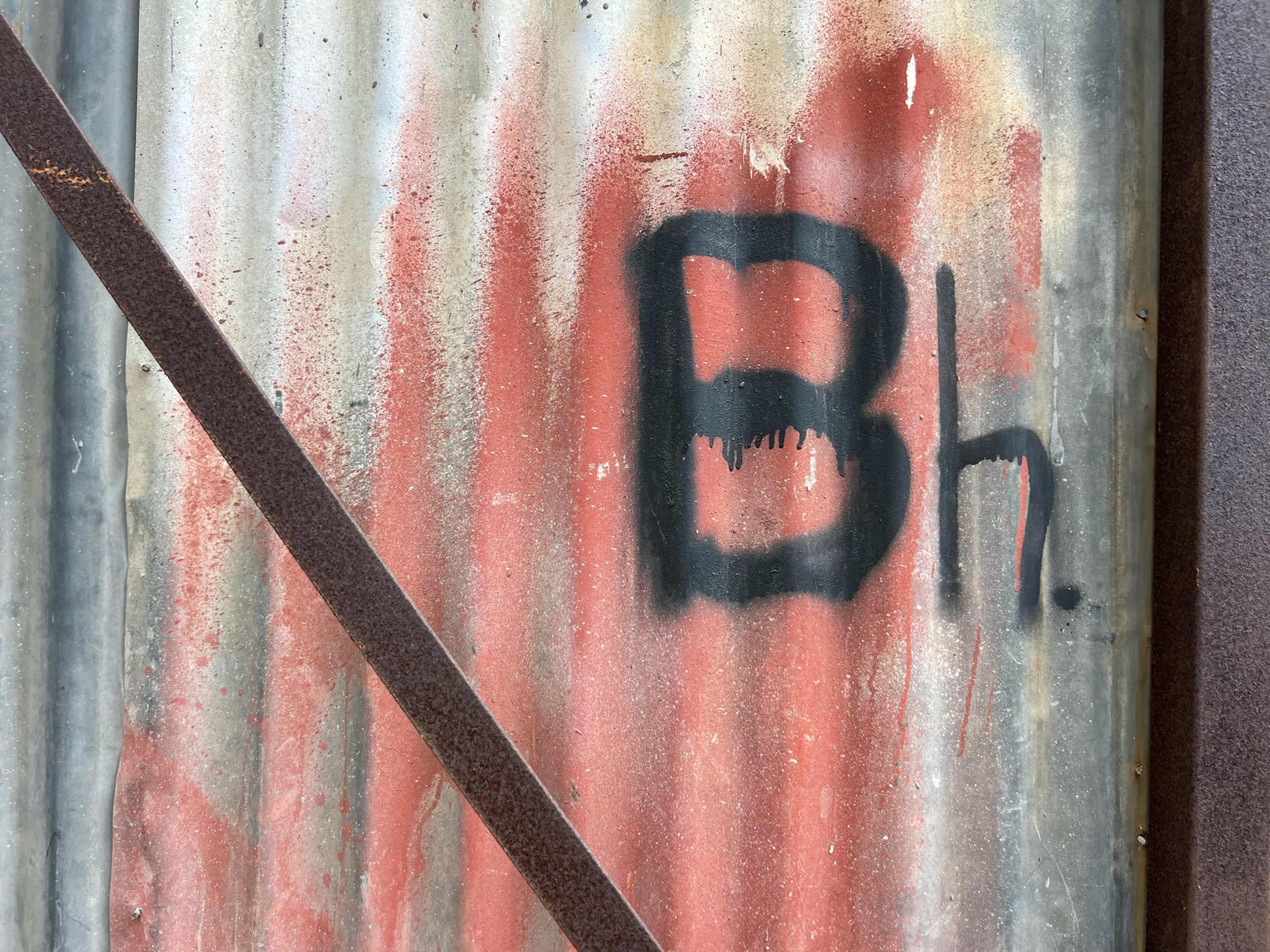 The image shows a section of corrugated metal with red spray paint and the letters "Bh." prominently displayed.