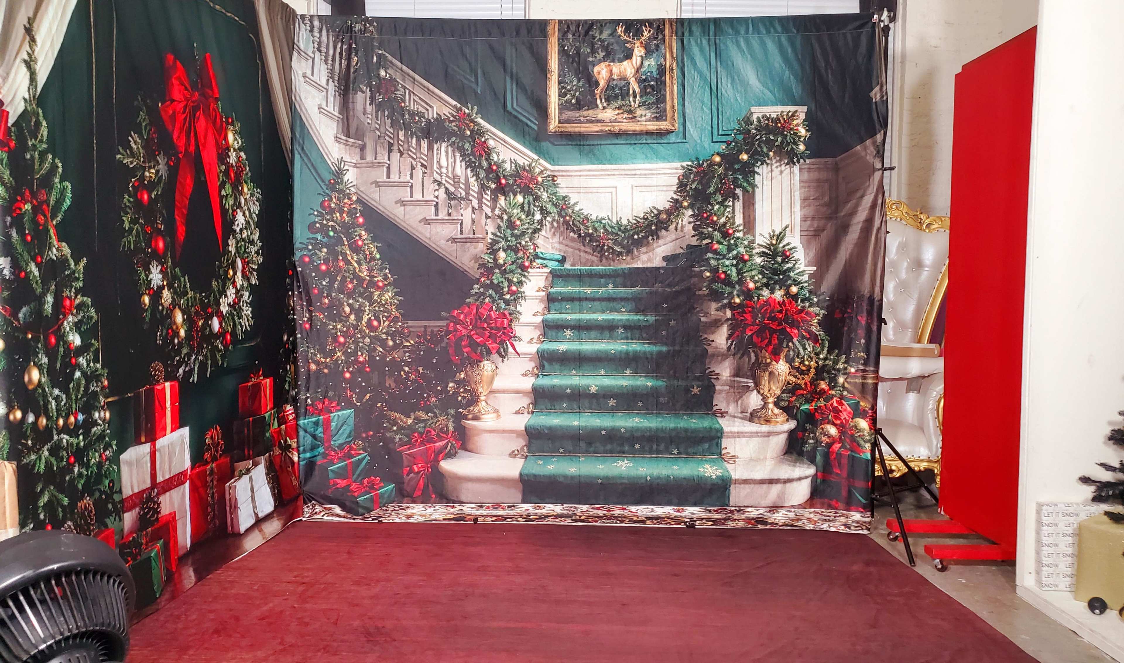 The image shows a decorated backdrop featuring a staircase adorned with festive greenery and red ribbons, surrounded by Christmas gifts.
