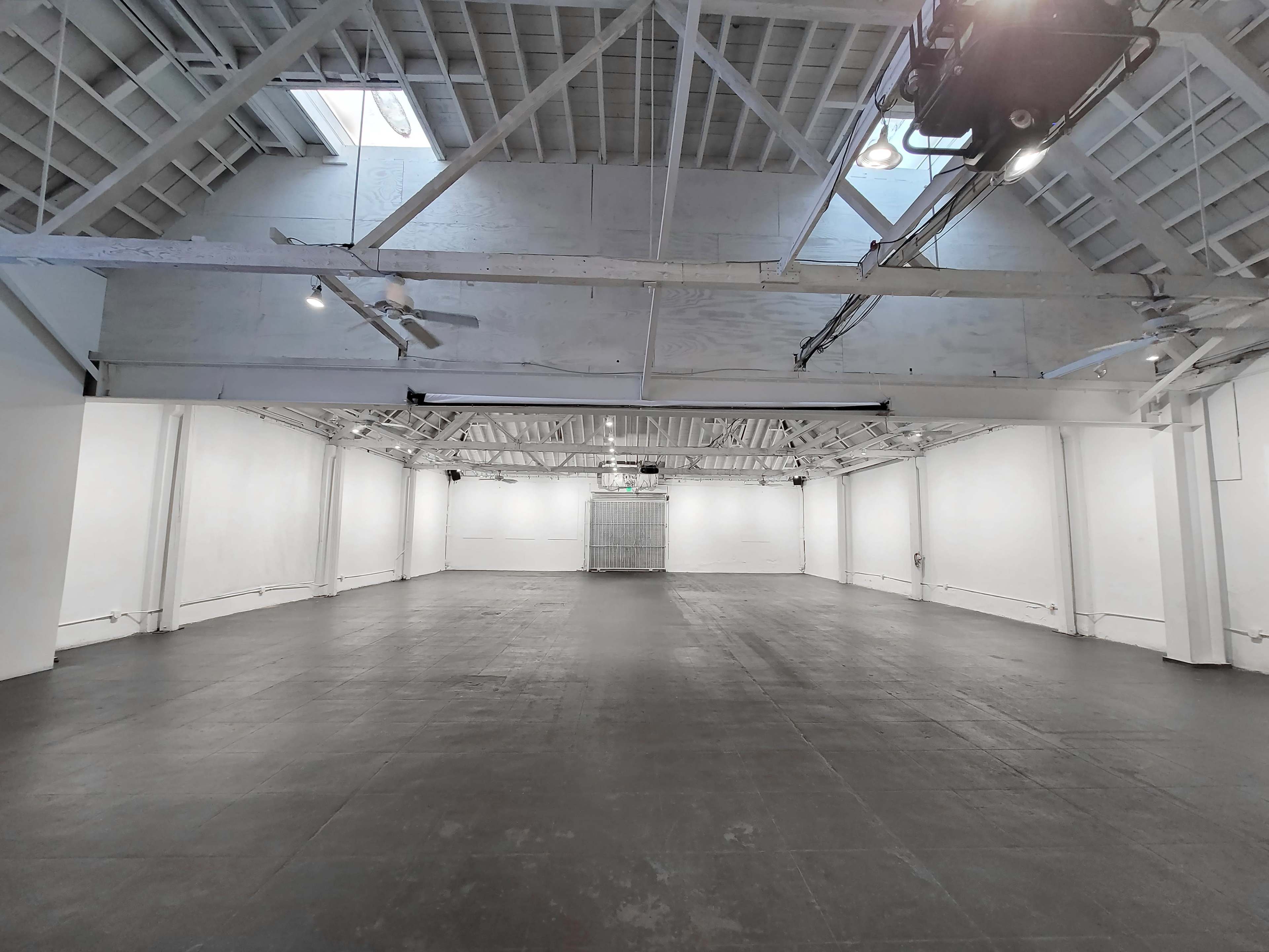 The image shows a spacious, empty industrial loft with high ceilings and white walls.