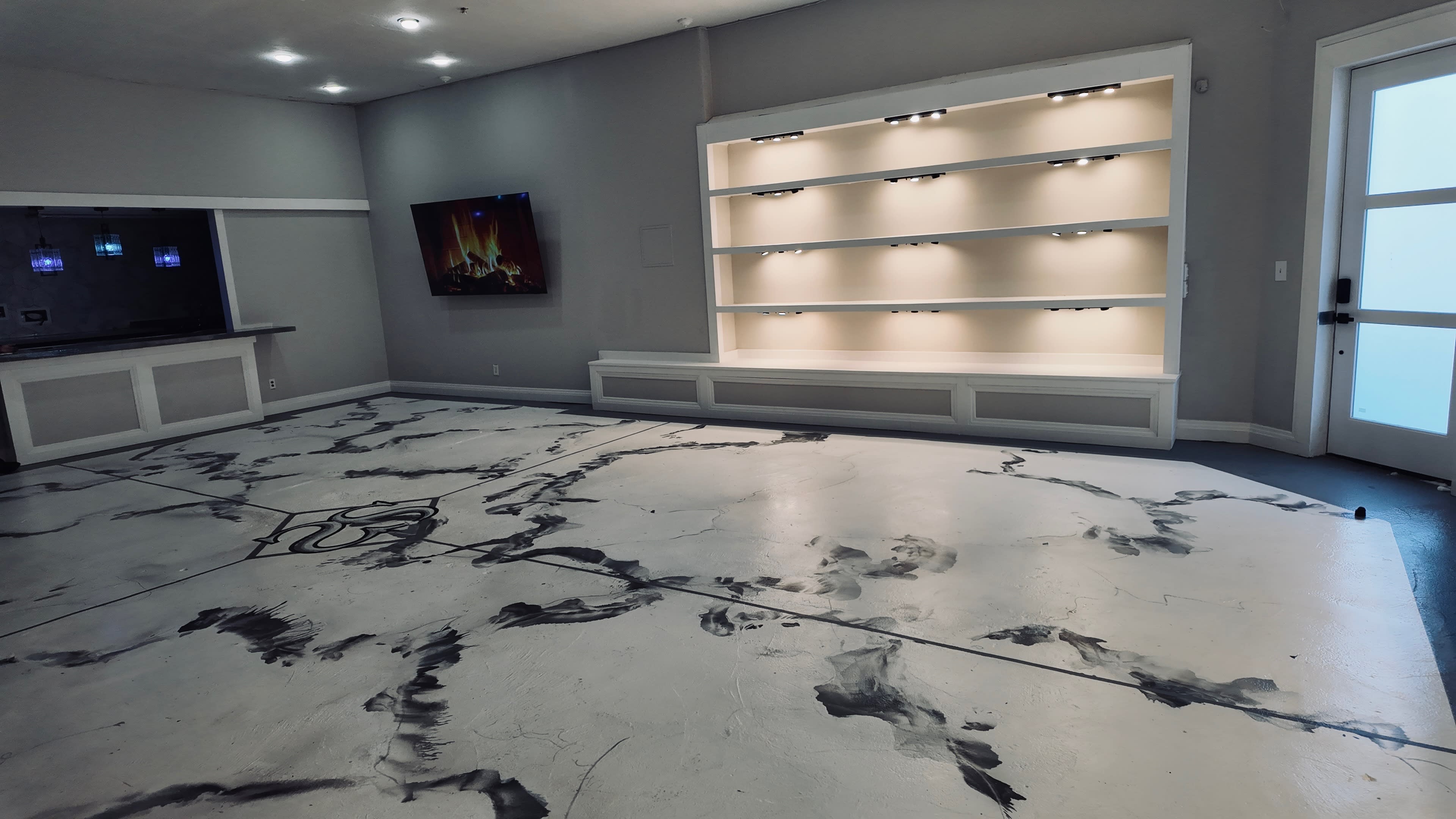 The image shows an interior space with a modern design featuring a polished floor with a marble-like pattern, a minimalist wall shelf with lighting, and a TV mounted on the wall.
