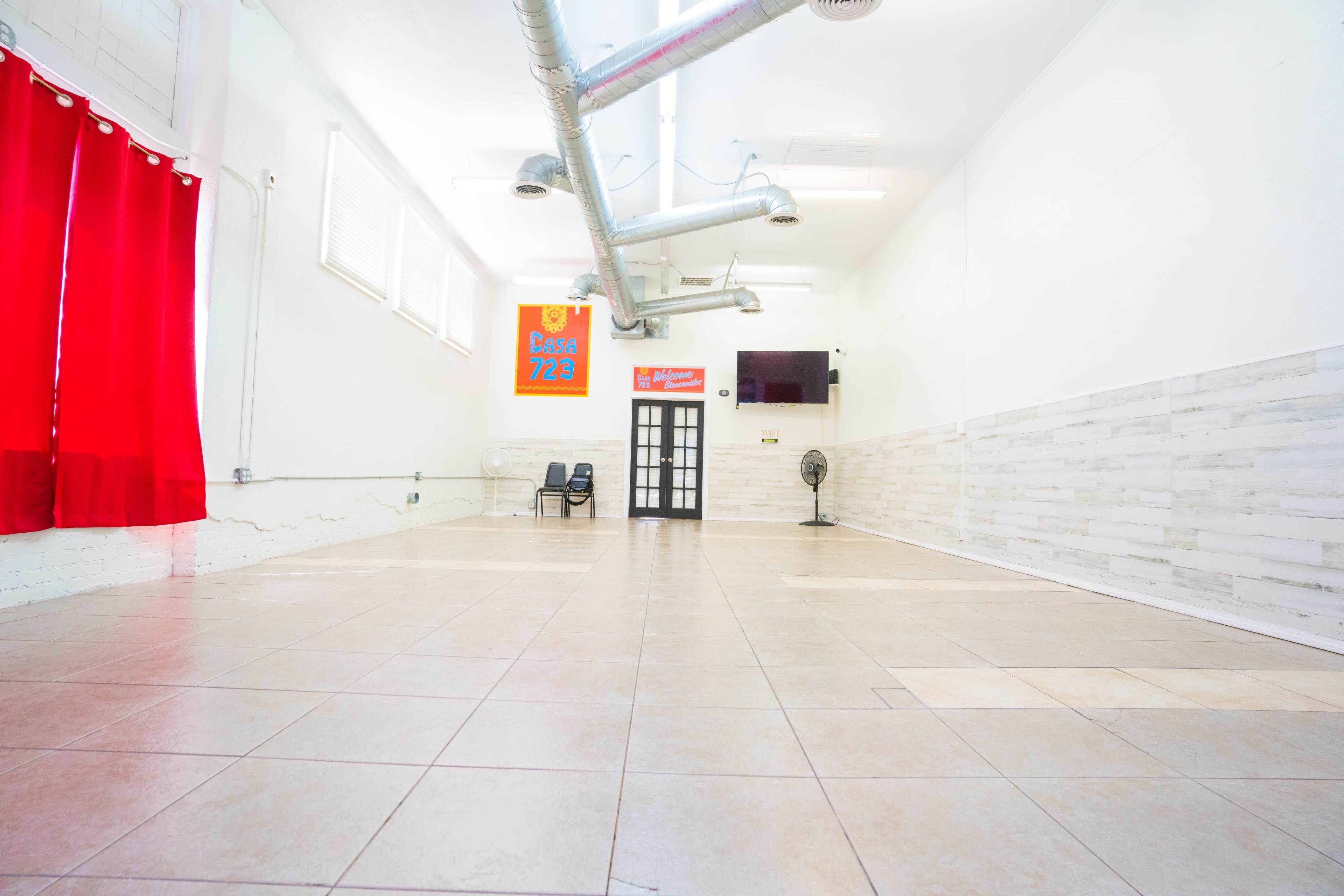 A spacious room with tiled flooring, white walls, a red curtain, and a few chairs against one wall.