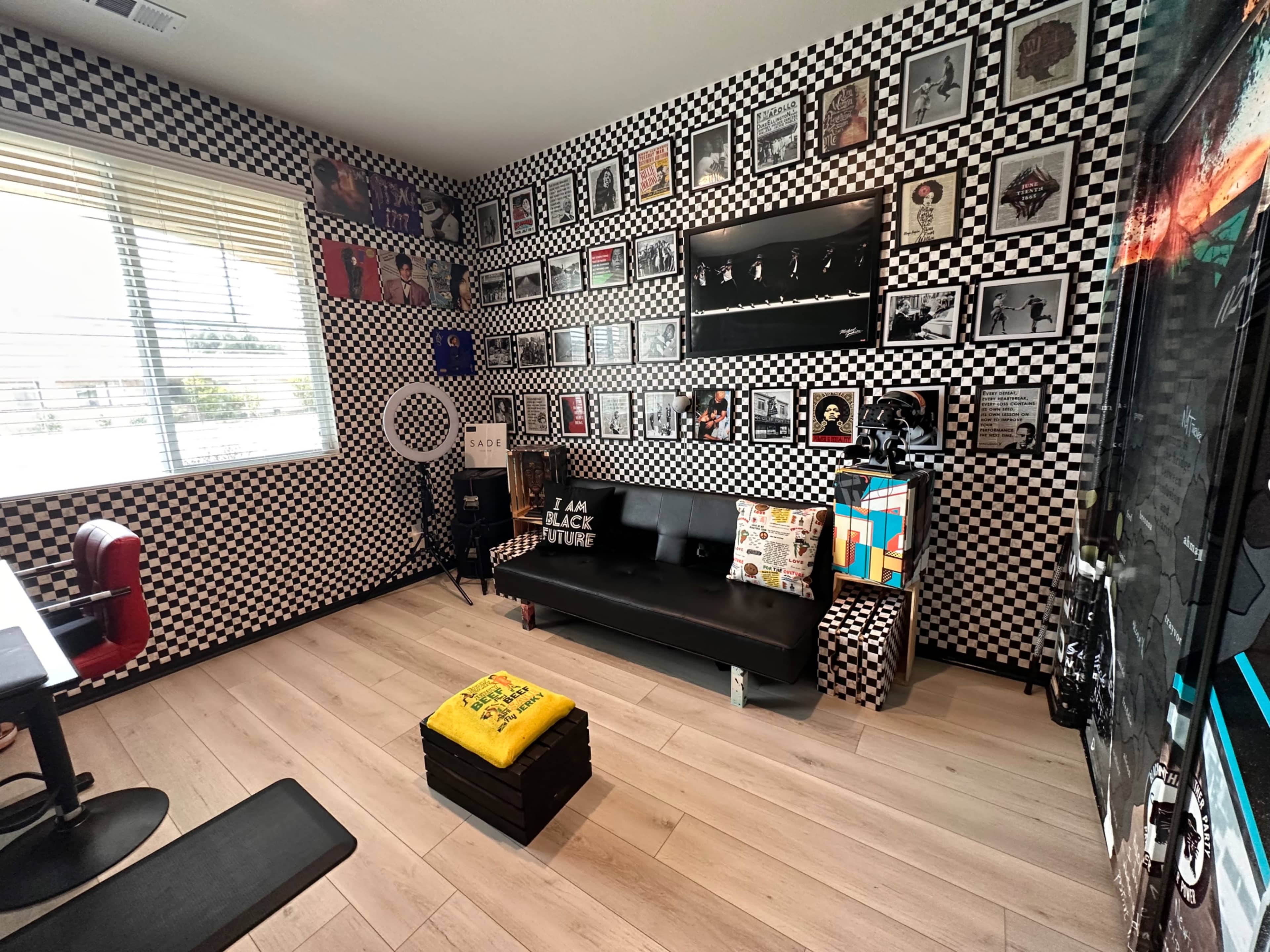 A room with checkered black and white walls, a black couch adorned with various cushions, and a collection of framed artworks displayed above it.