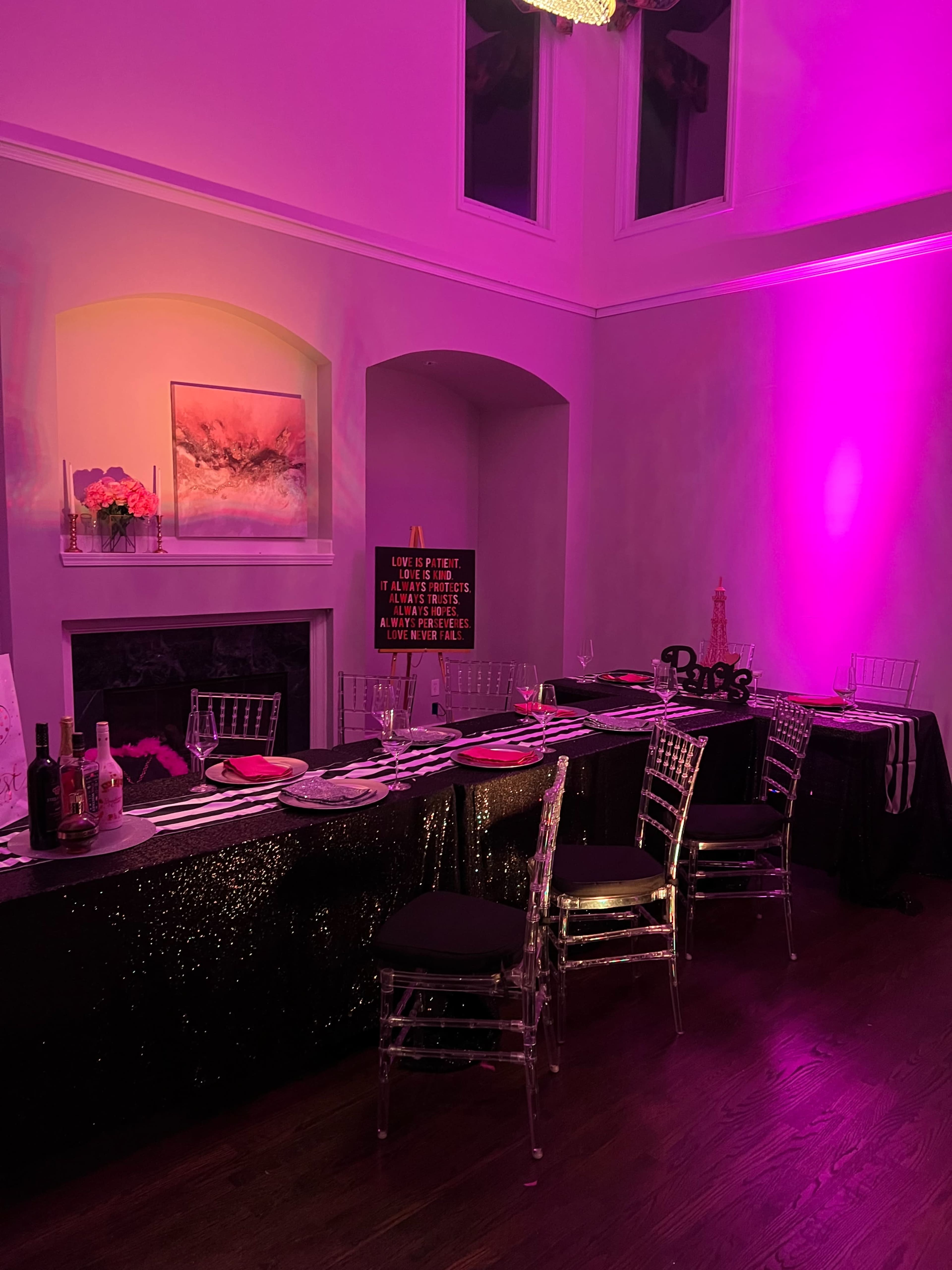 A dining setup with a black and purple color scheme, featuring a long table adorned with decorative items, chairs, and a lit fireplace in the background.