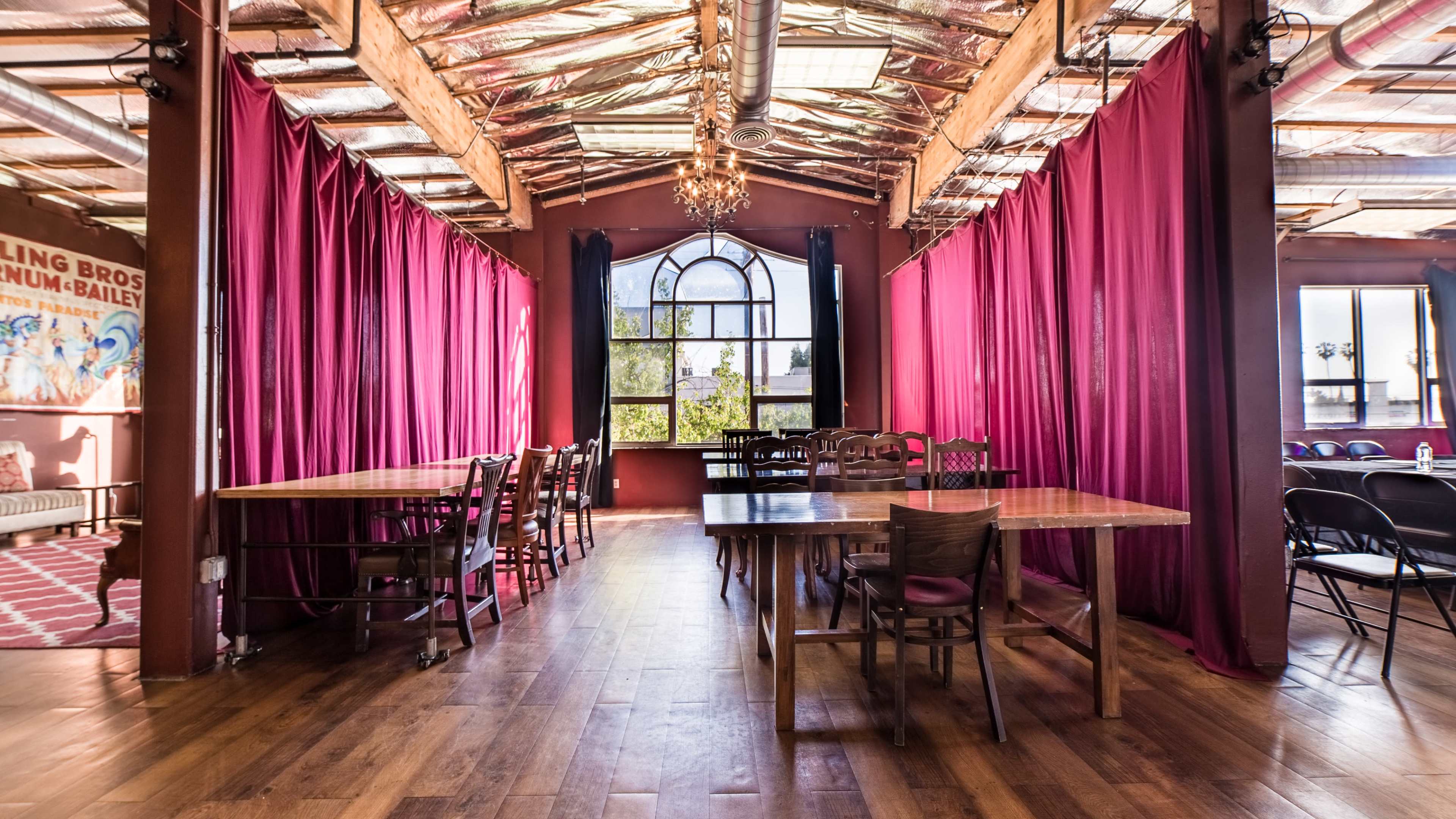 A spacious room with wooden floors, several long tables, and maroon curtains along the walls.