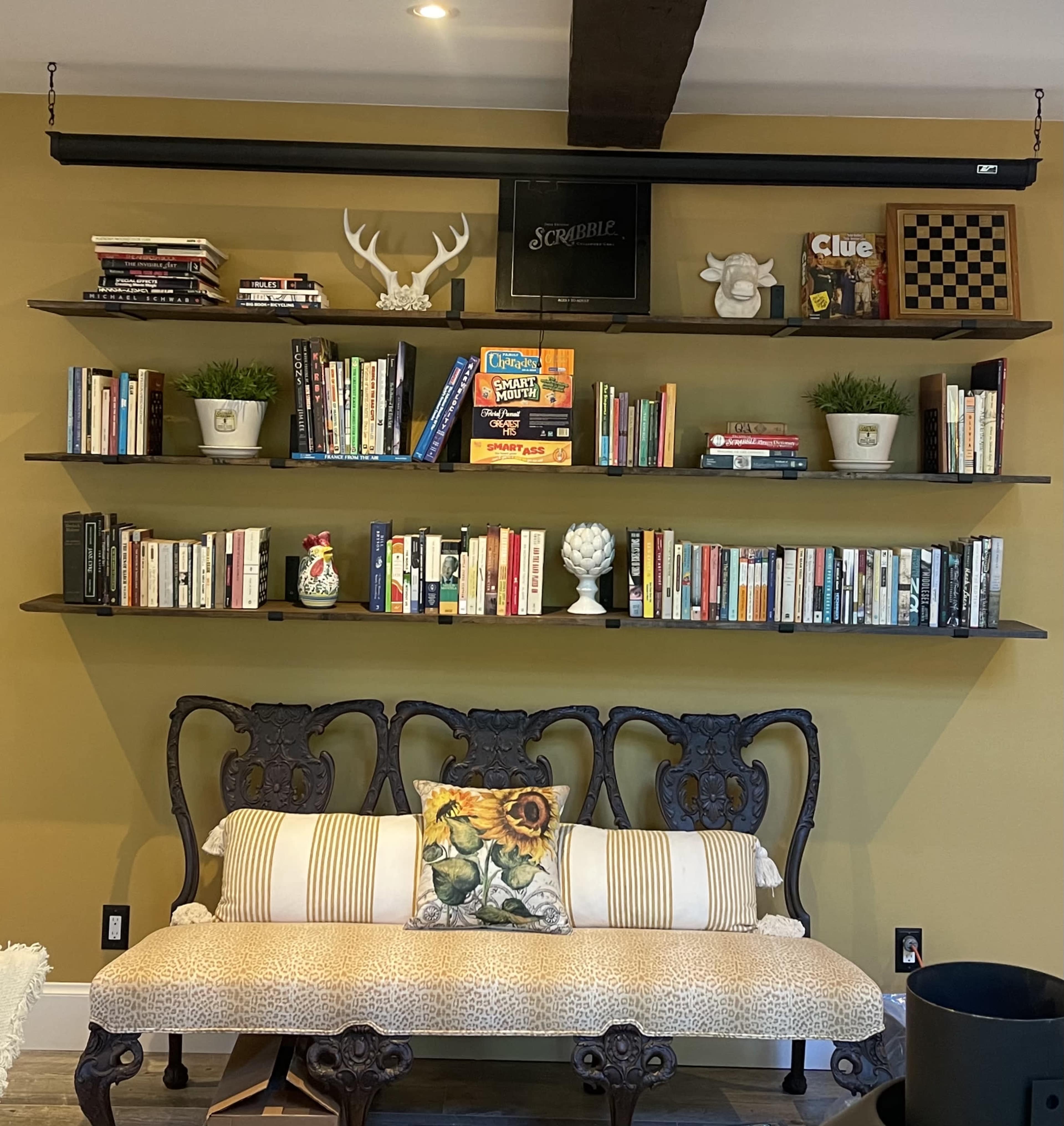 A wooden bench with patterned upholstery sits in front of a wall-mounted shelf filled with books and decorative items.