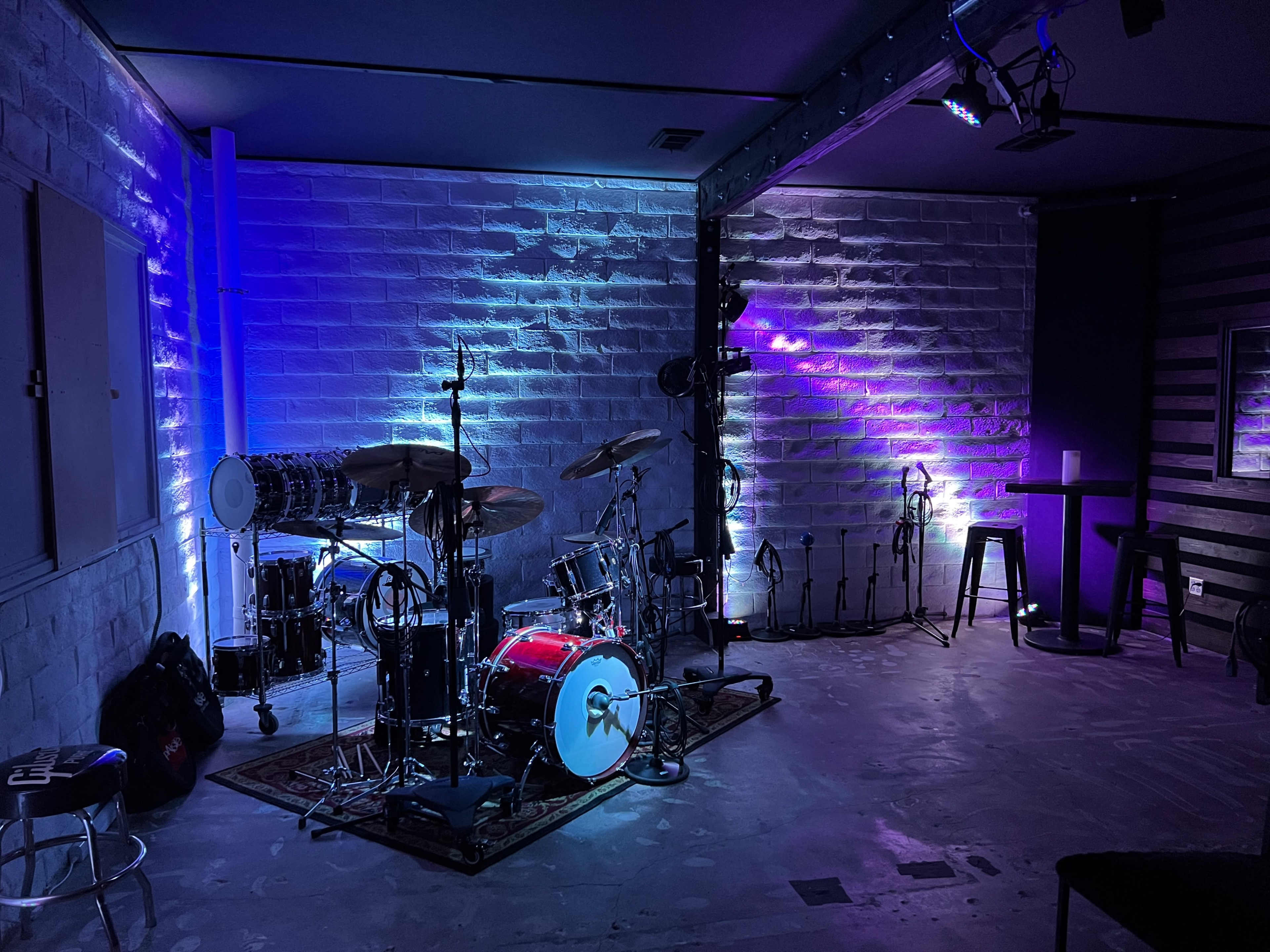 A music performance space features a drum set surrounded by illuminated walls and equipment stands.