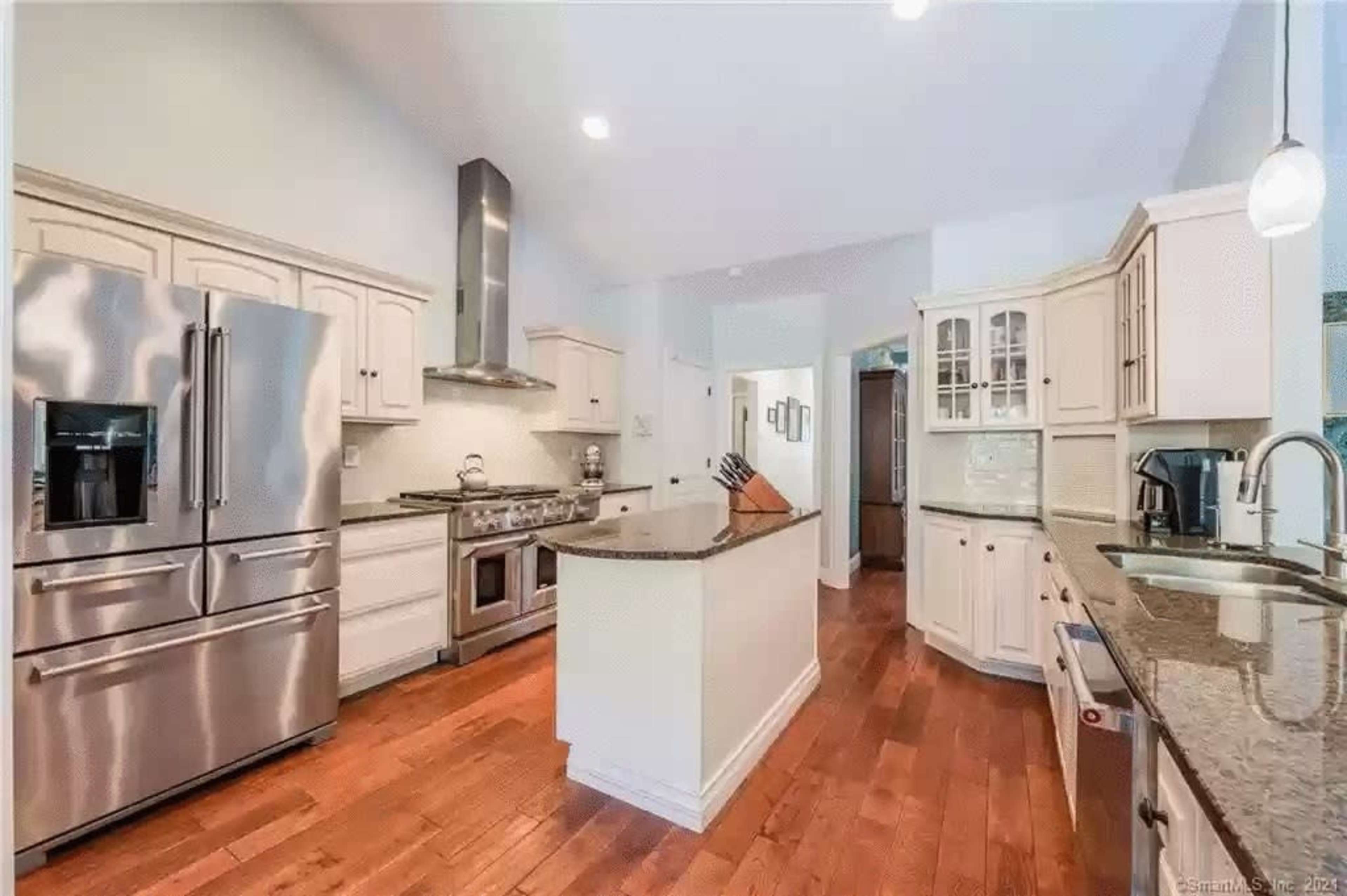 A modern kitchen with stainless steel appliances, wooden flooring, and light-colored cabinetry.