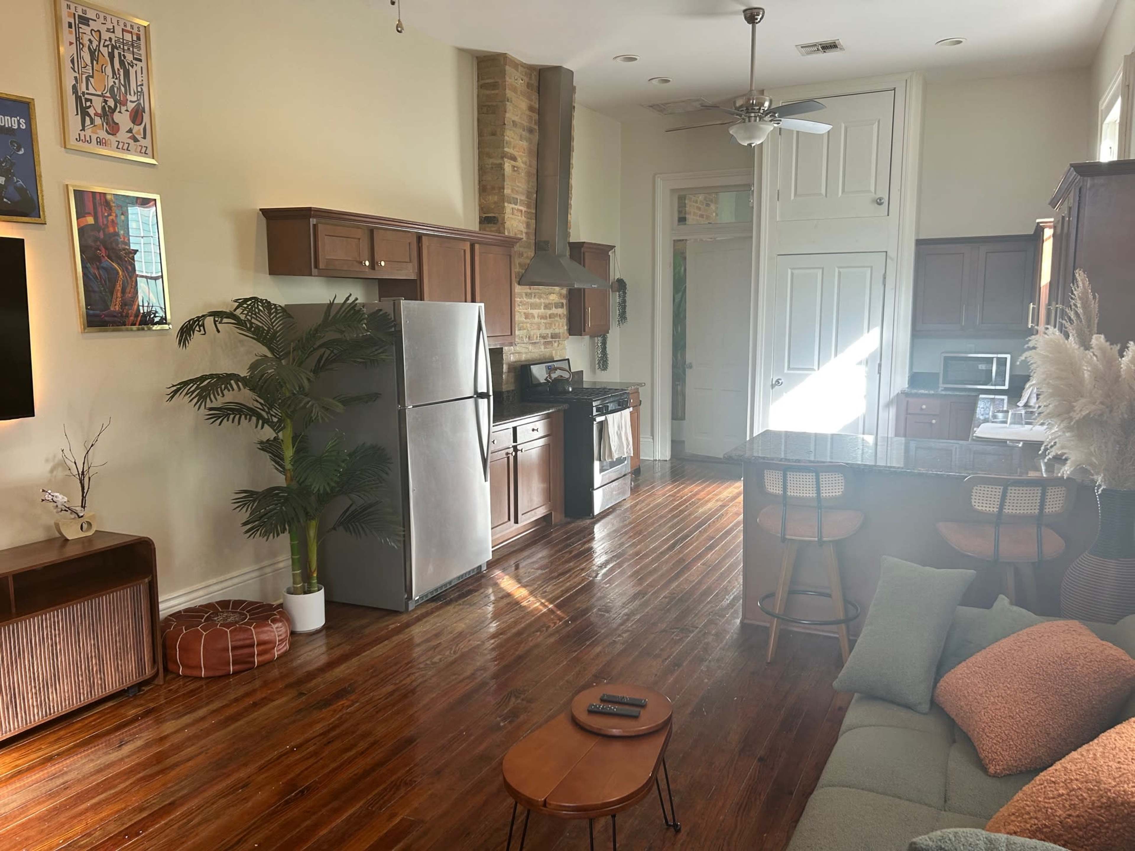 The image shows a spacious kitchen and living area with wooden flooring, modern appliances, and a seating area.