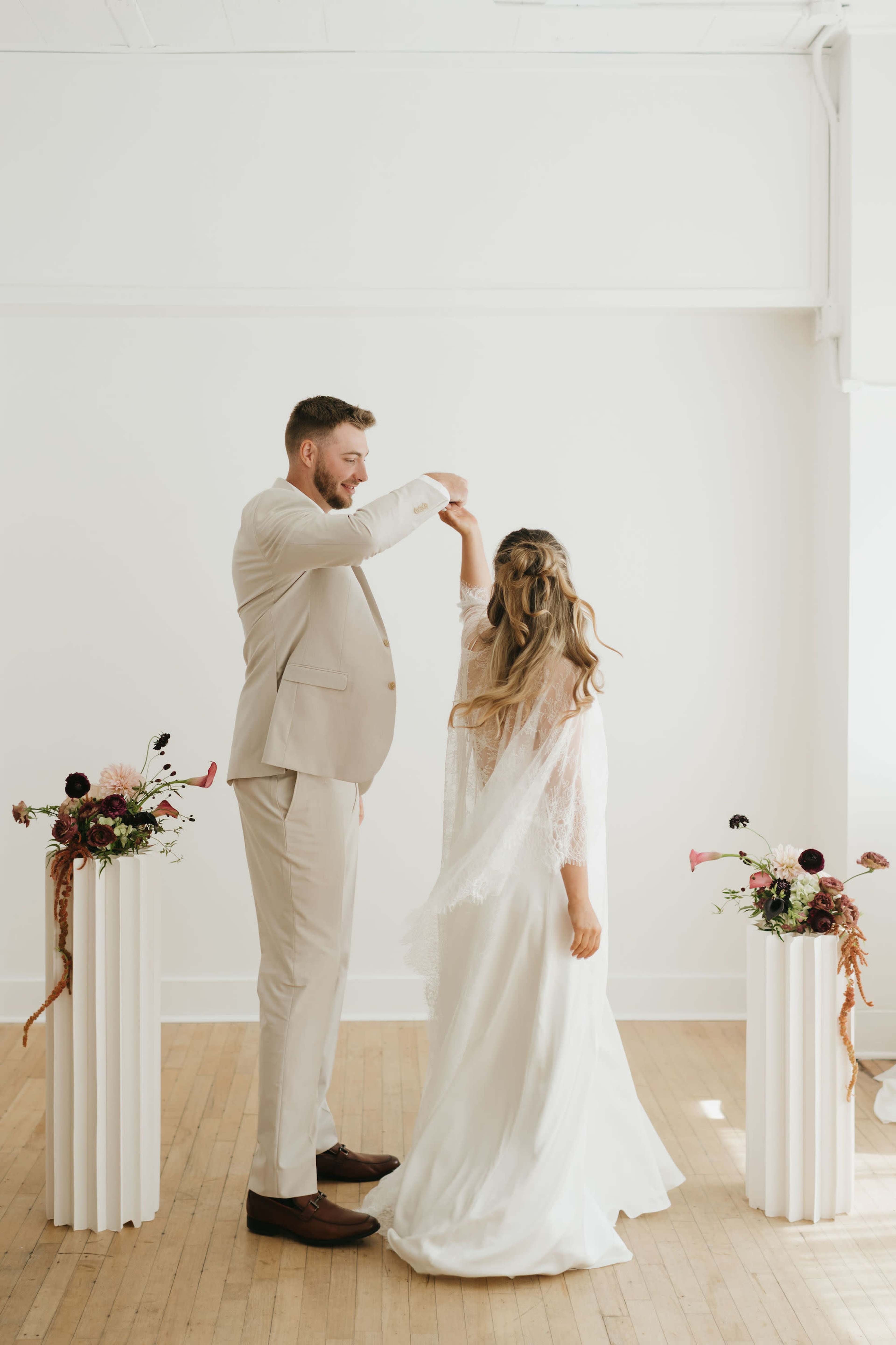 A couple dances together in a minimalist interior, surrounded by floral arrangements on pedestal stands.