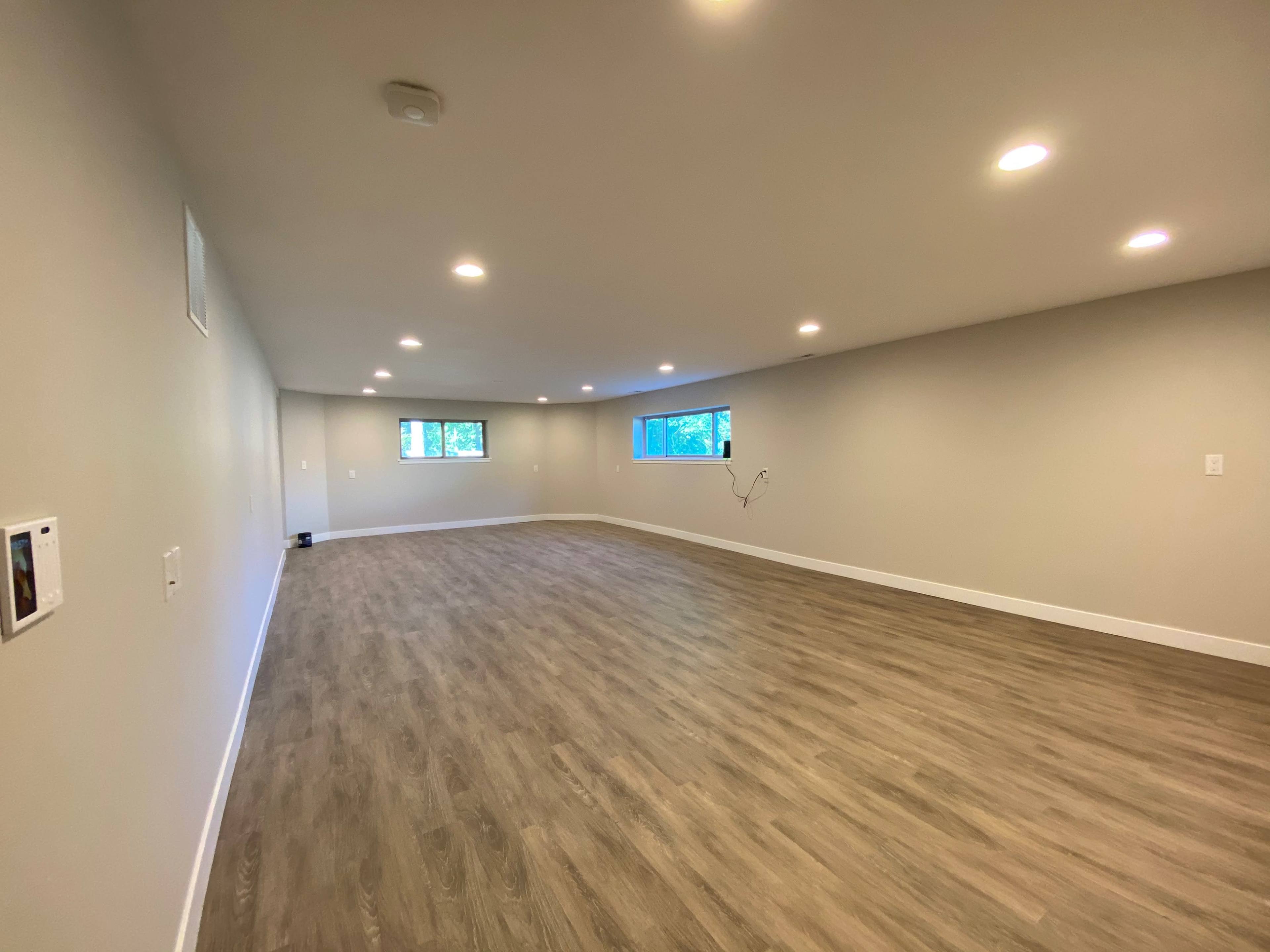 The image shows an empty room with wood-like flooring, light walls, and multiple recessed lights illuminating the space.
