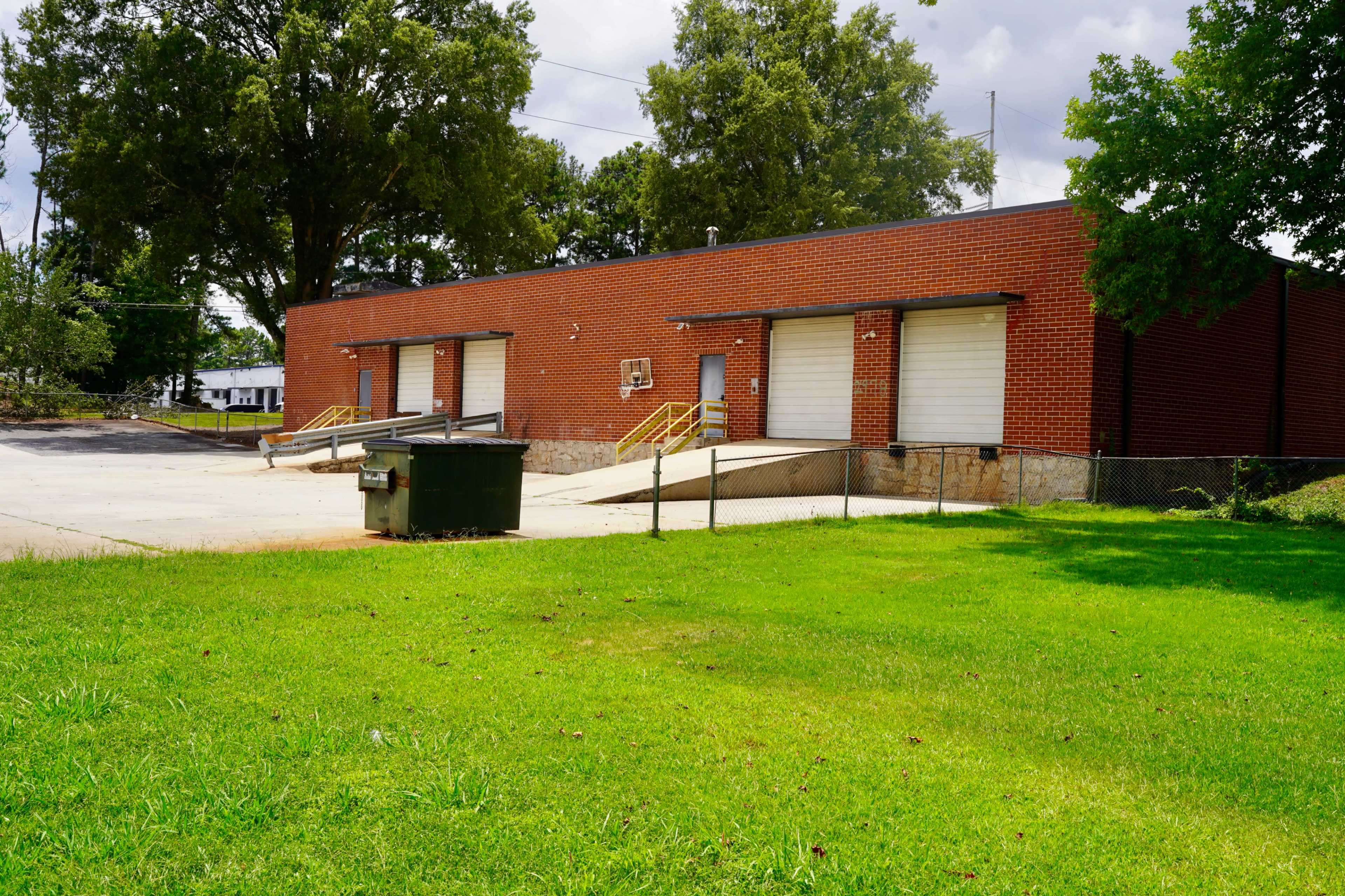 A brick building with loading docks and a green dumpster is located on a grassy area.