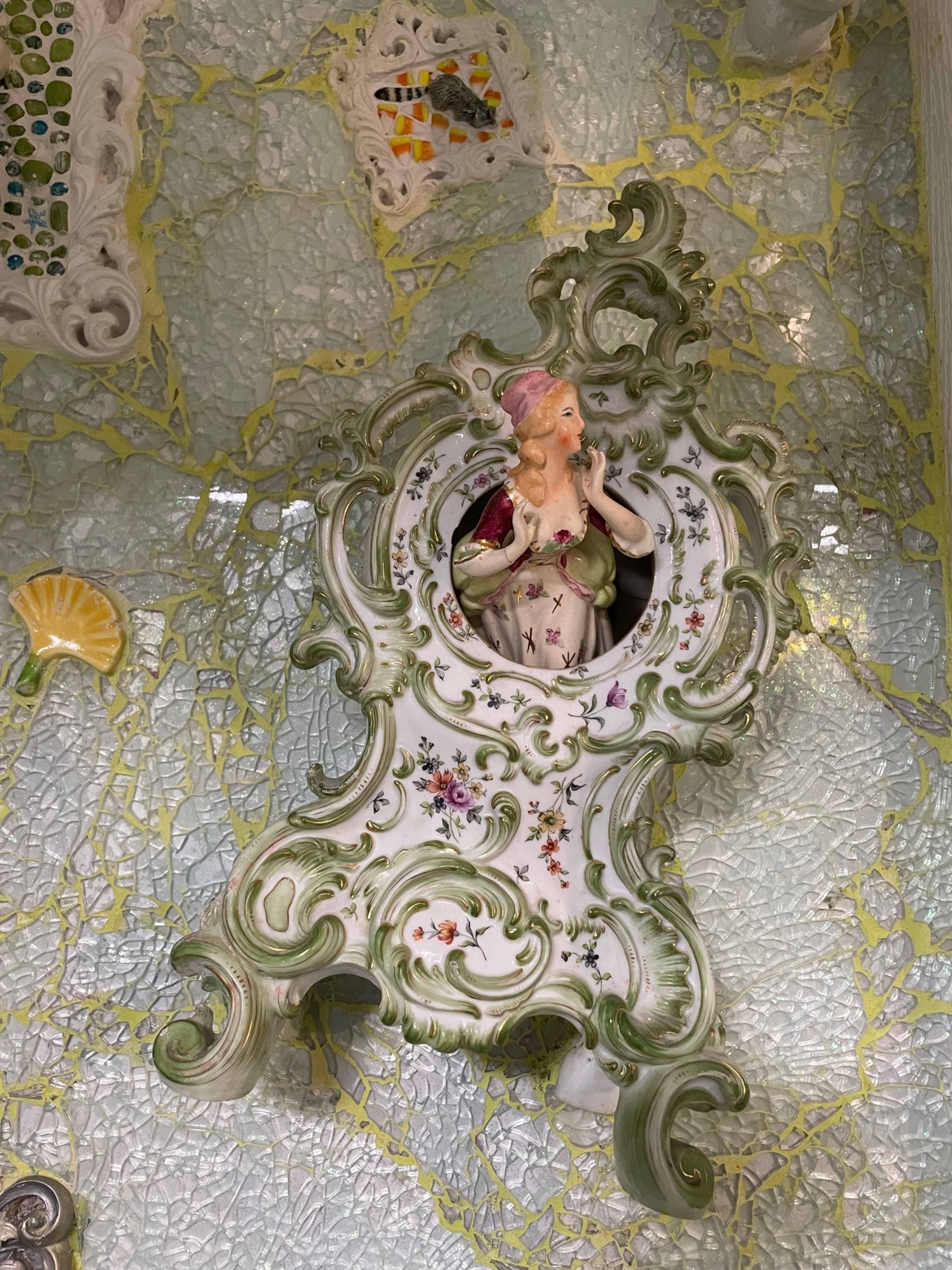 An ornate porcelain figurine of a woman set within a decorative, intricately designed wall piece.