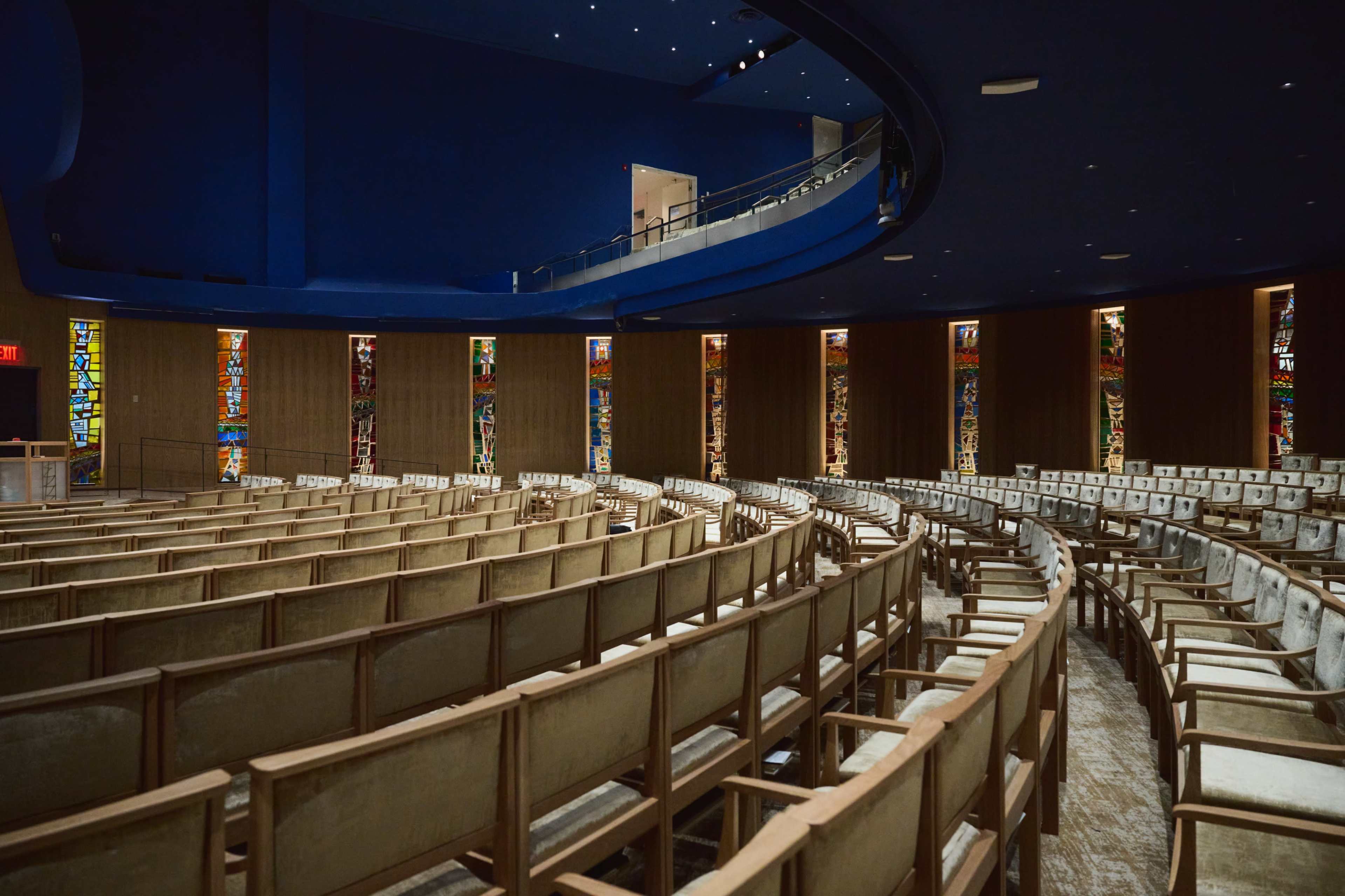 A circular auditorium with rows of wooden seats and colorful stained glass windows lining the walls.