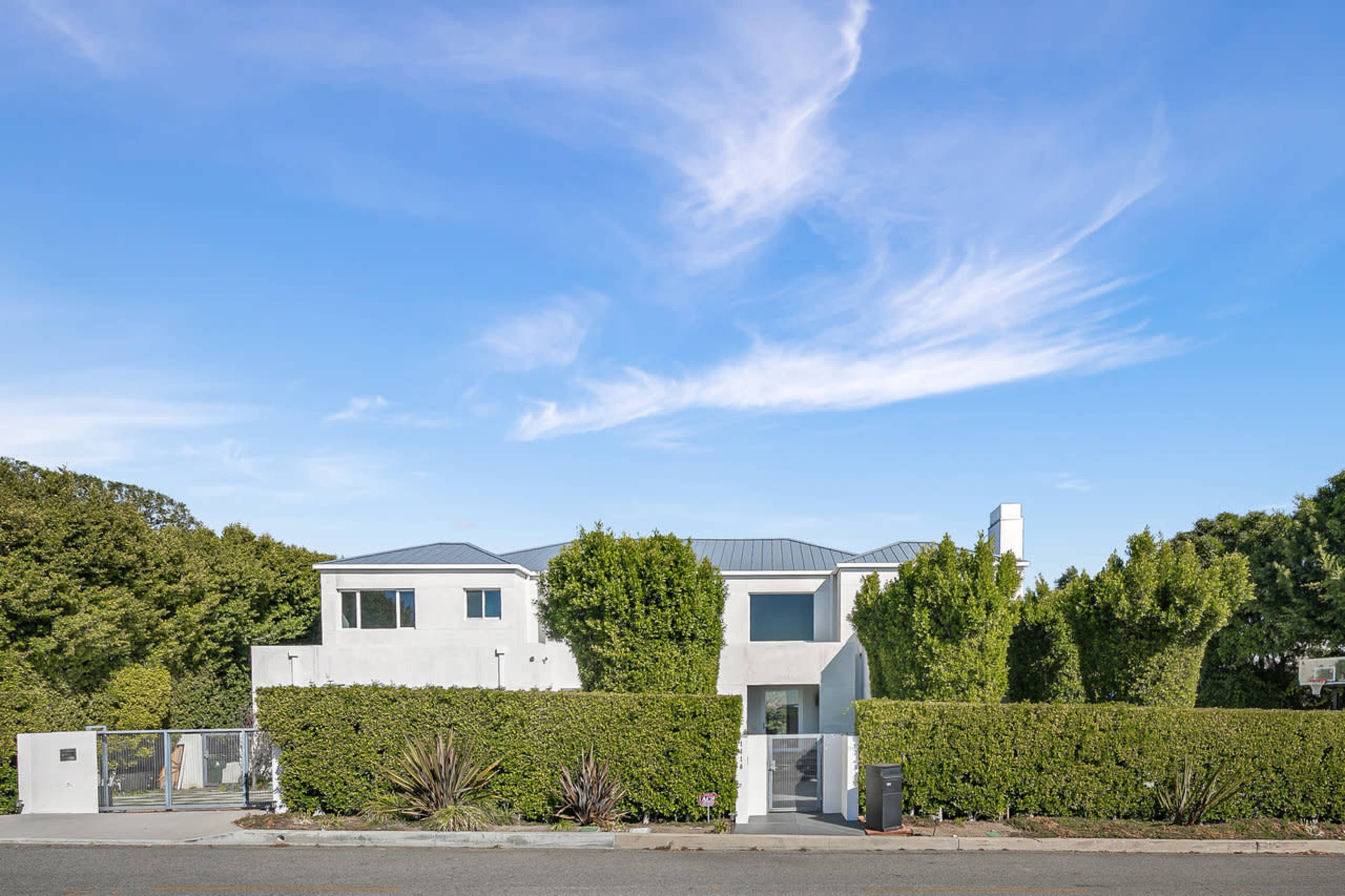 A modern two-story house is surrounded by tall hedges under a clear blue sky.