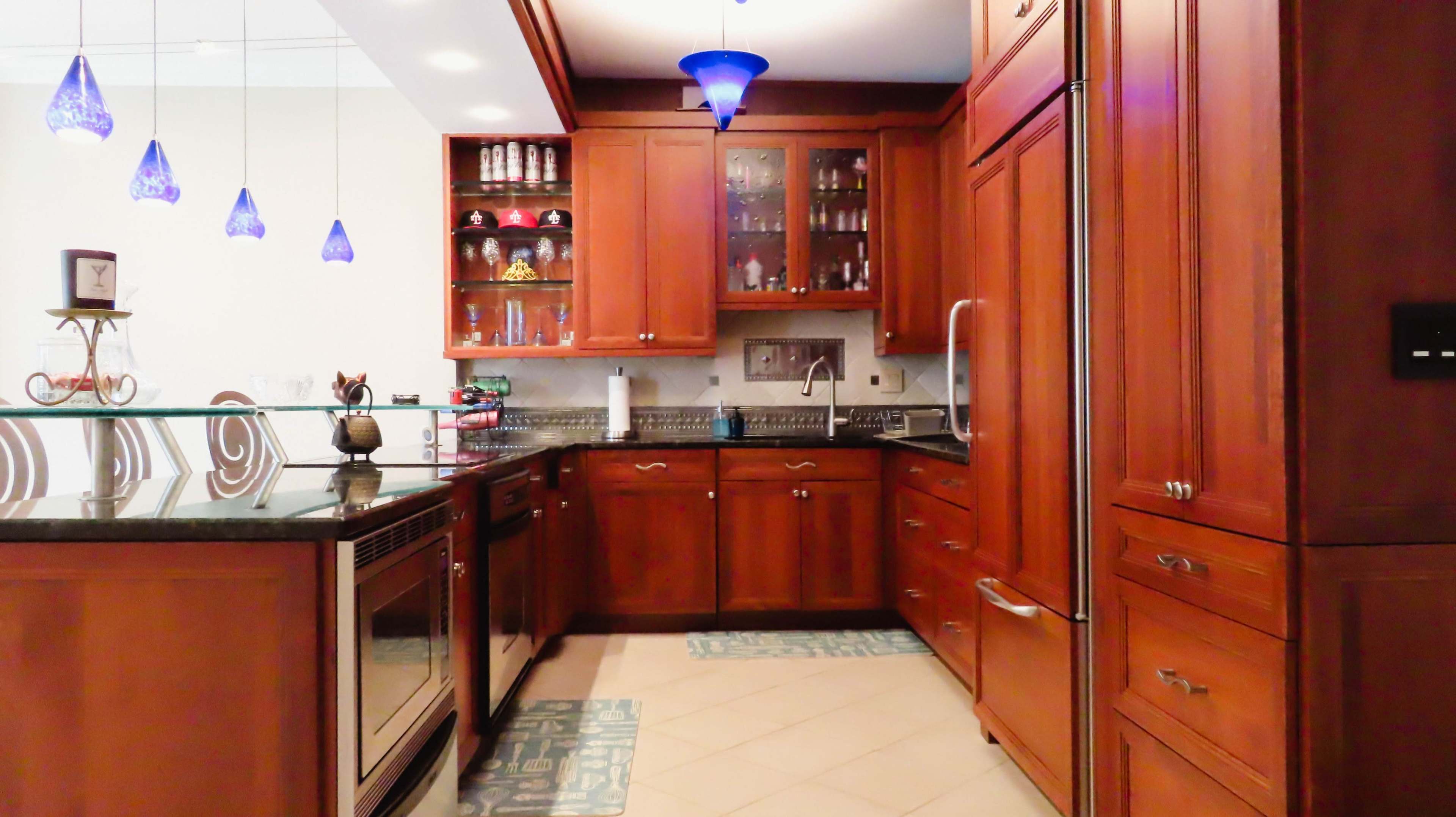 A modern kitchen features wooden cabinetry, stainless steel appliances, and blue pendant lights above the island.