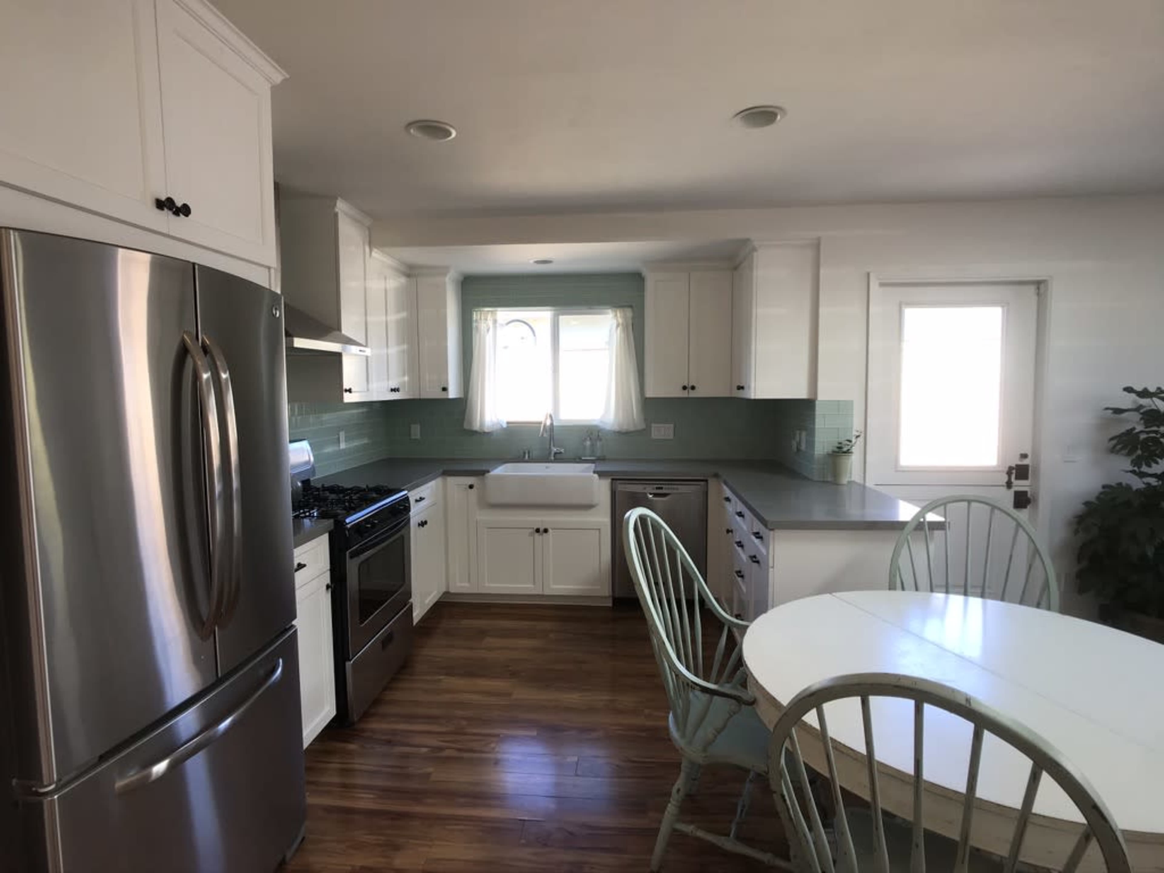 A modern kitchen featuring stainless steel appliances, a large sink, white cabinetry, and a round dining table with green chairs.