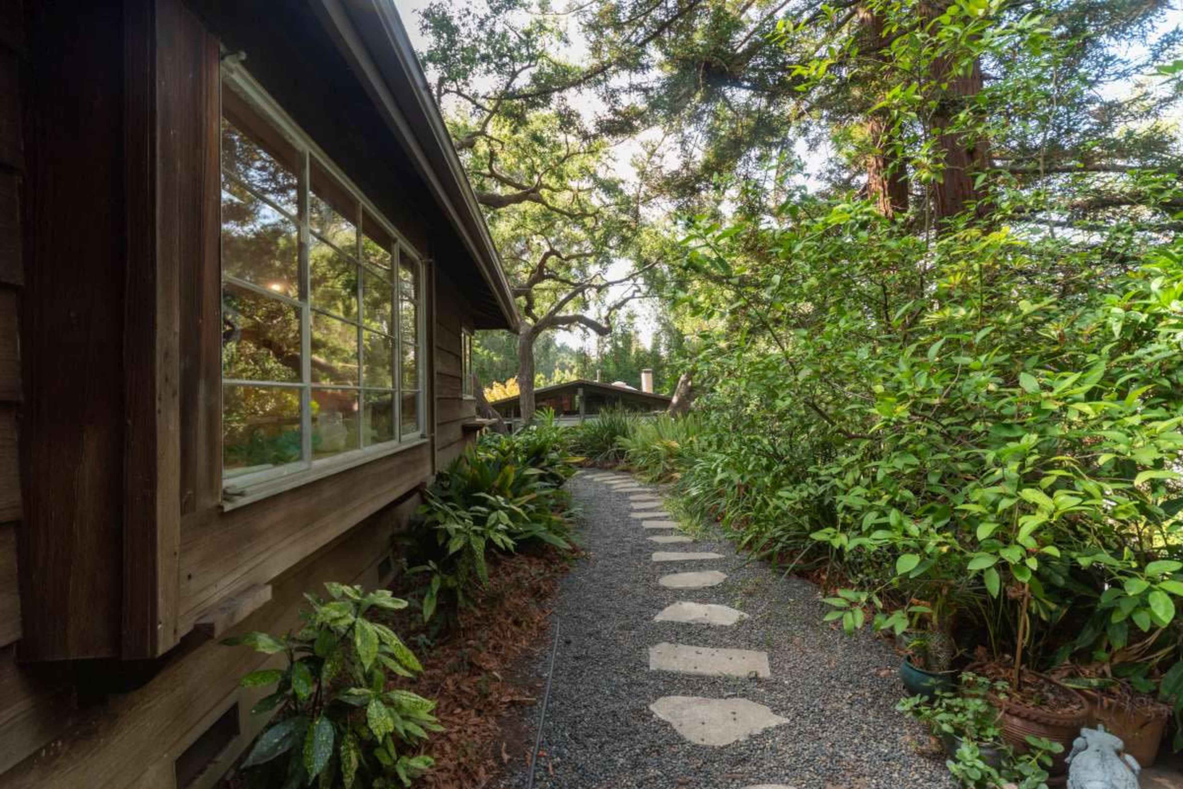 A stone pathway winds through lush greenery beside a wooden cabin.