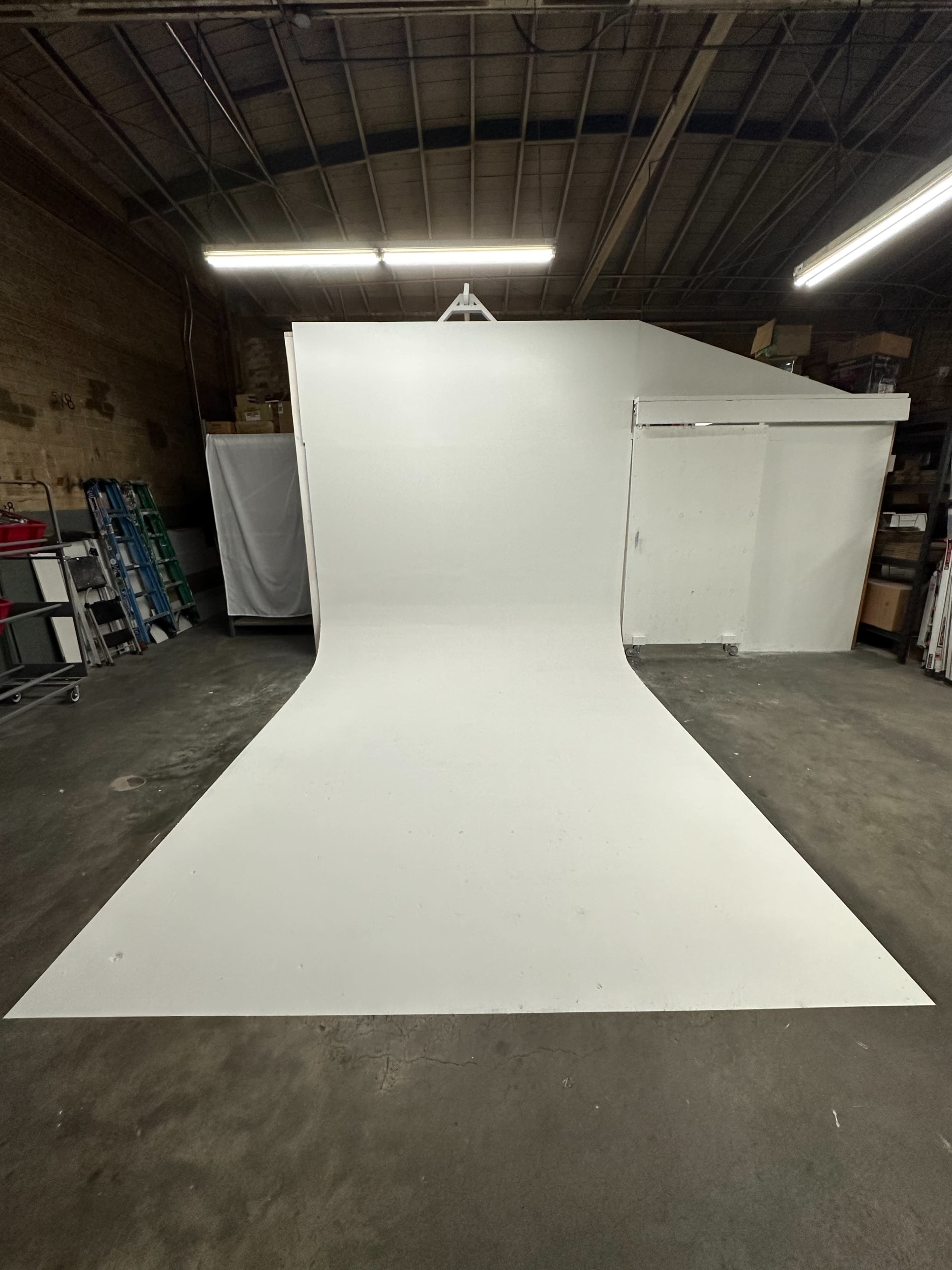 The image shows a spacious studio with a white backdrop that includes a curved floor and surrounding storage areas.