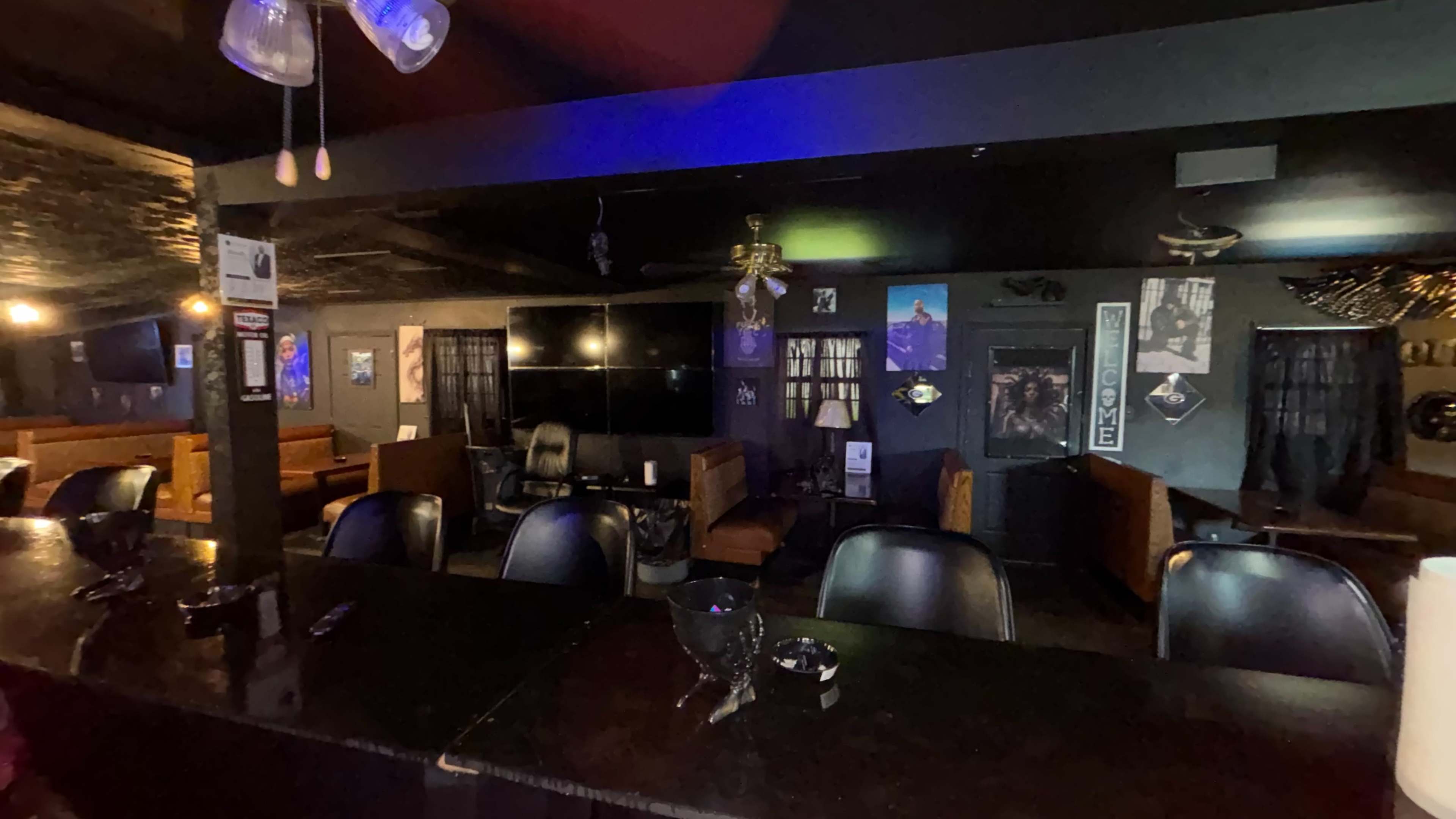 A dimly lit bar area features a long wooden counter with chairs, surrounded by lounge seating and wall decorations.
