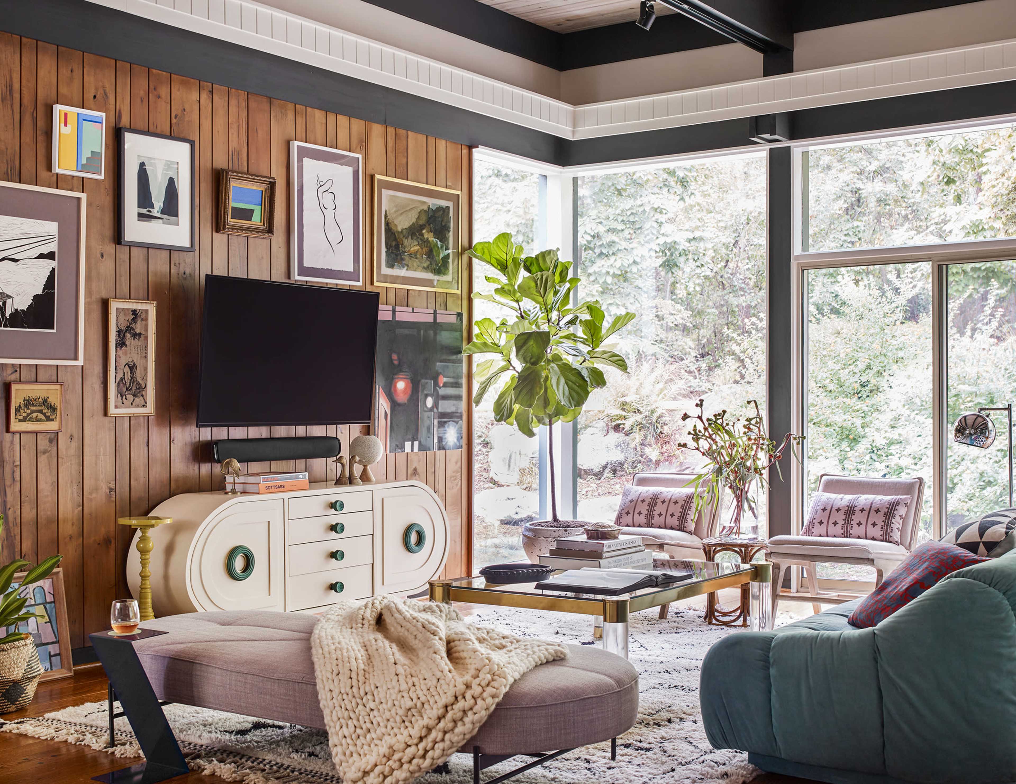 The living room features a combination of wood-paneled walls, various framed artworks, a modern television, a large indoor plant, and comfortable seating areas.