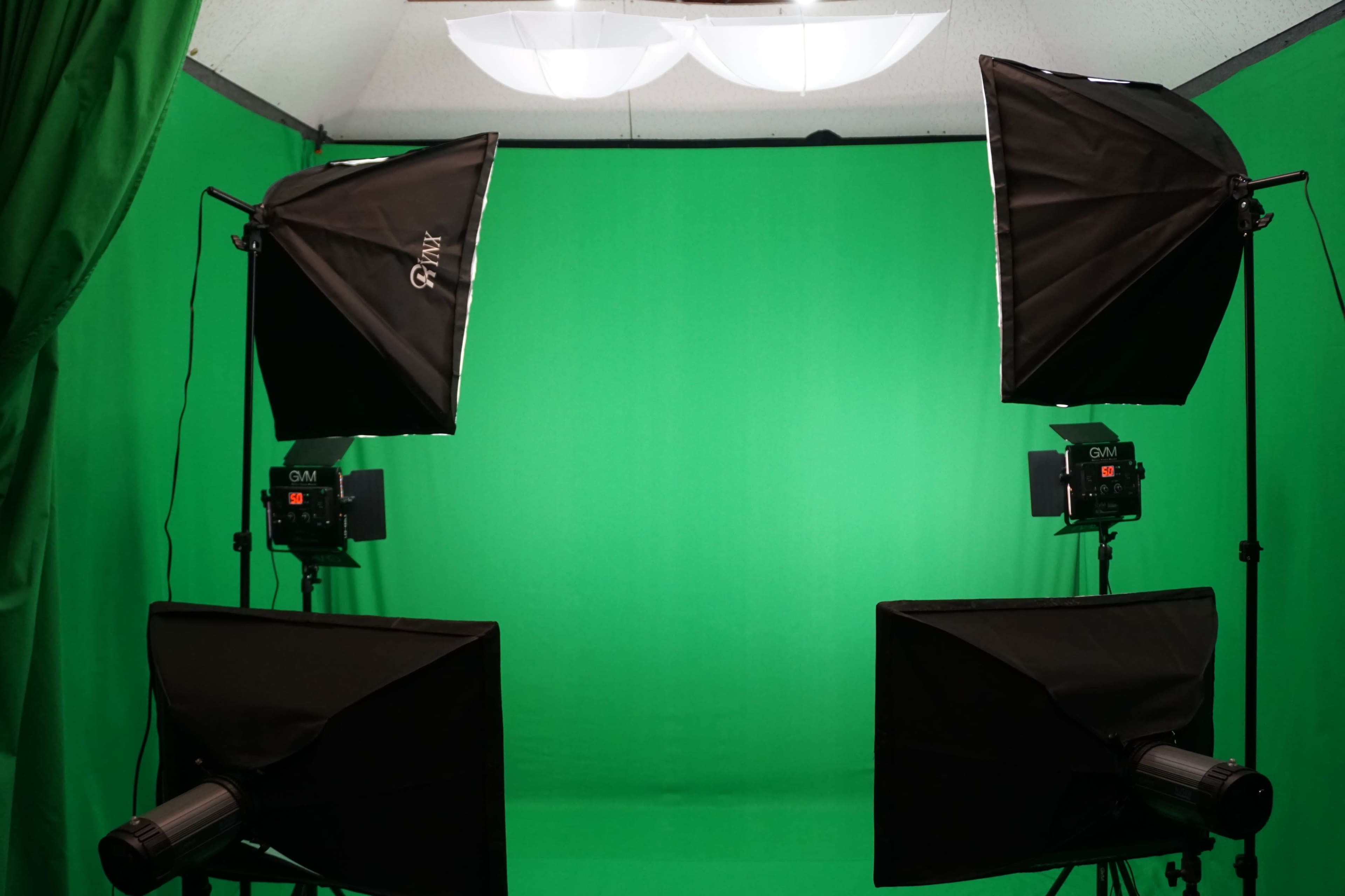 A photography setup with two softbox lights positioned on either side of a green backdrop, complemented by two black monitors in front.