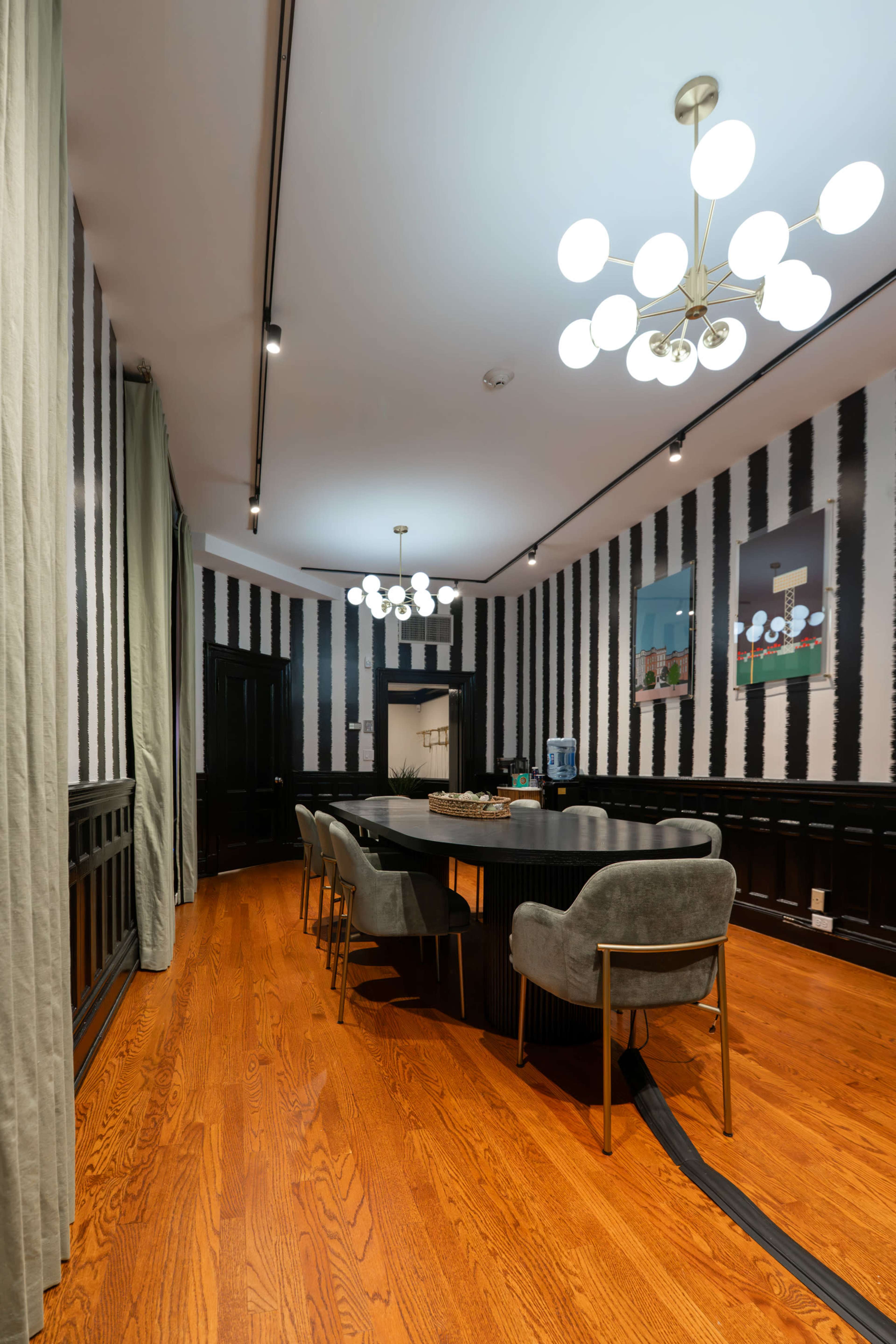 The image shows a modern conference room featuring a long black table, gray chairs, and striped walls illuminated by multiple round ceiling lights.