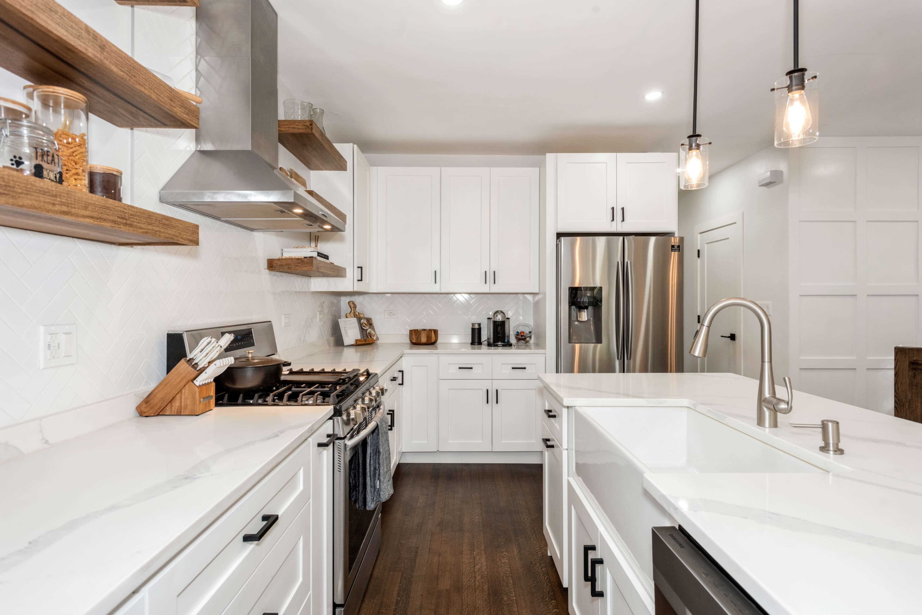 A modern kitchen featuring white cabinetry, stainless steel appliances, and wooden shelves with decorative items.