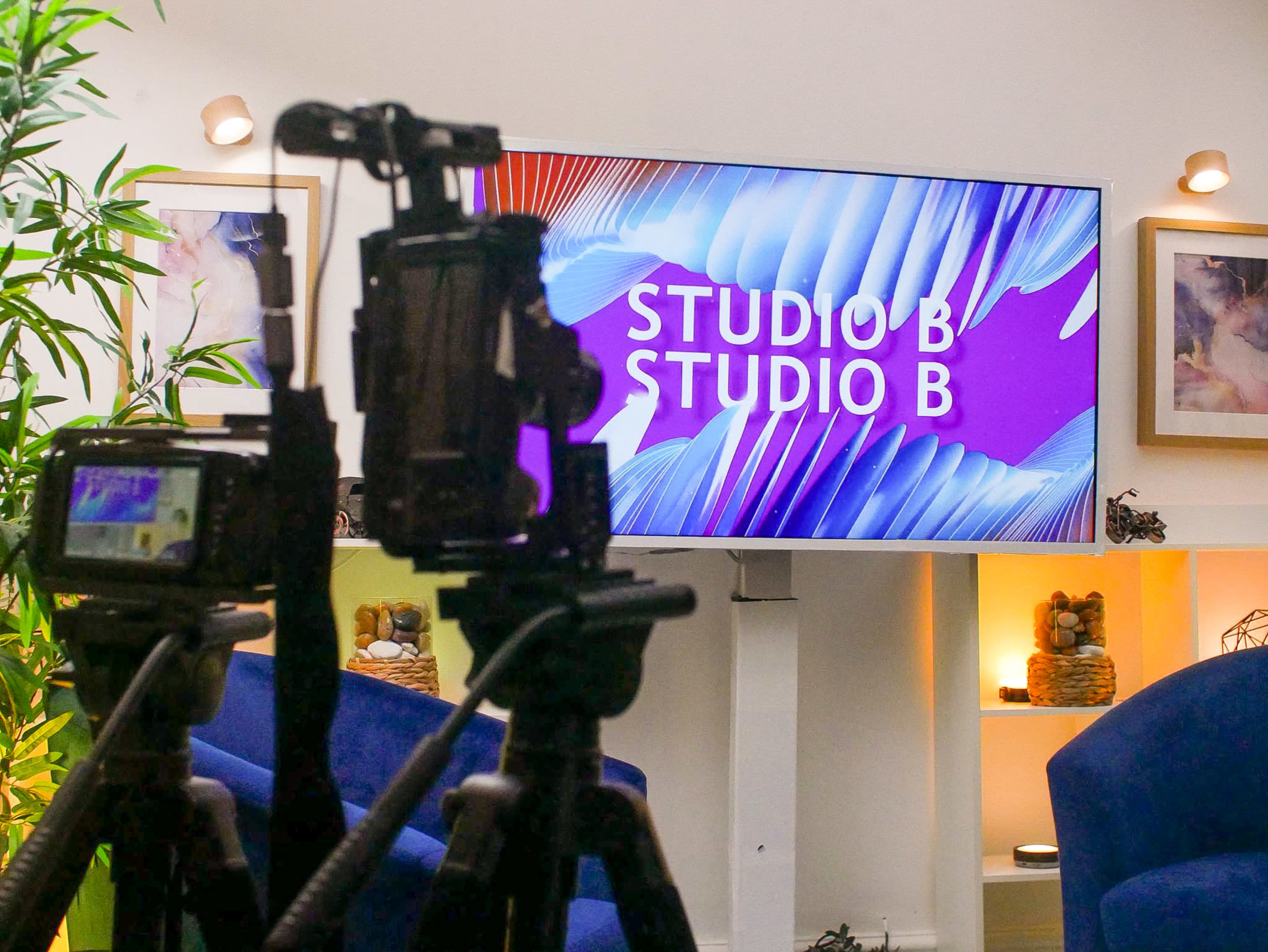 The image shows a television screen displaying the text "STUDIO B" in a modern studio setup, with two cameras positioned in the foreground.