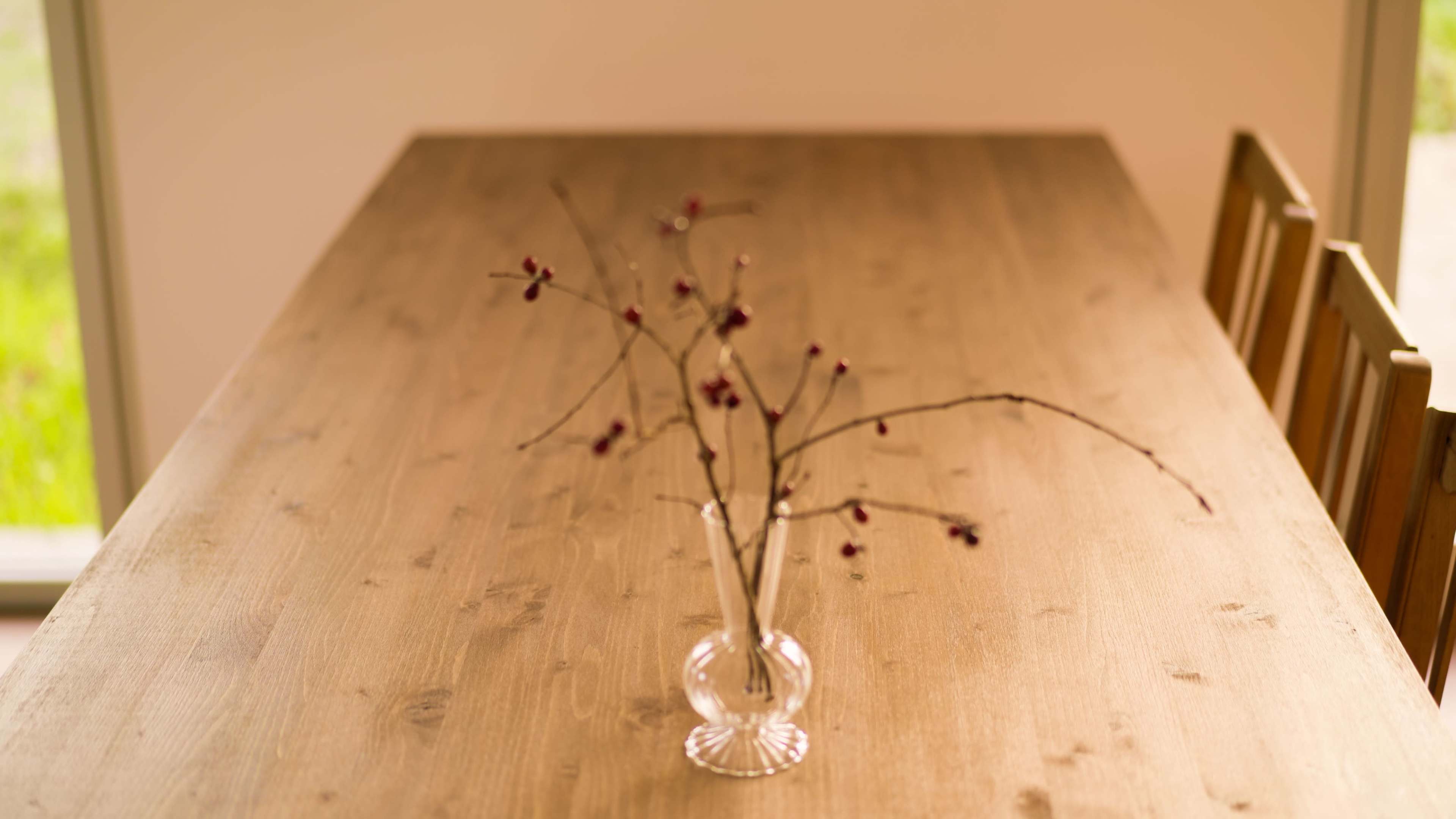 A clear vase with bare twigs and red berries stands on a wooden table.