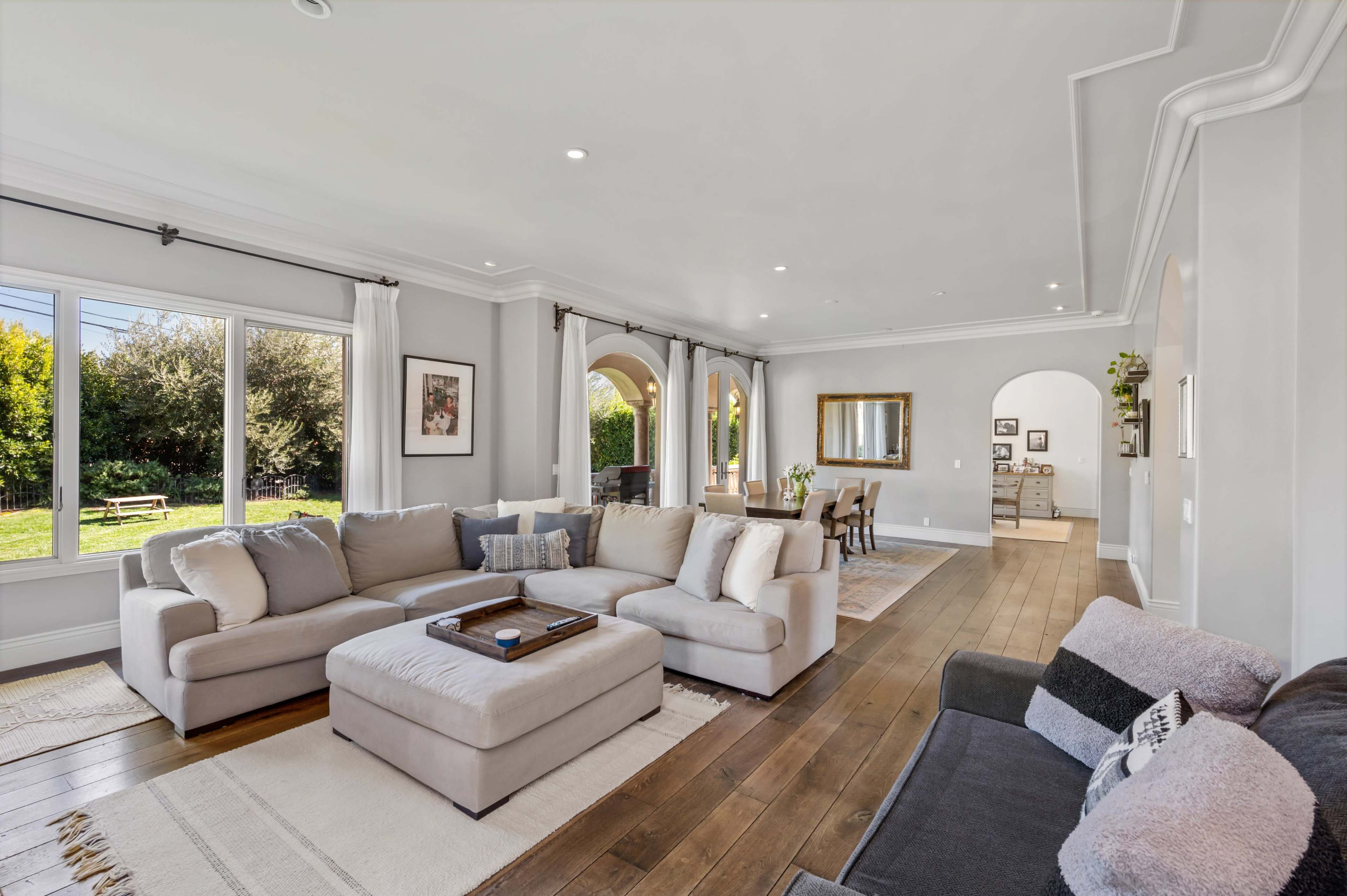 A spacious living room with a large sectional couch, a coffee table, and large windows overlooking a green outdoor area.