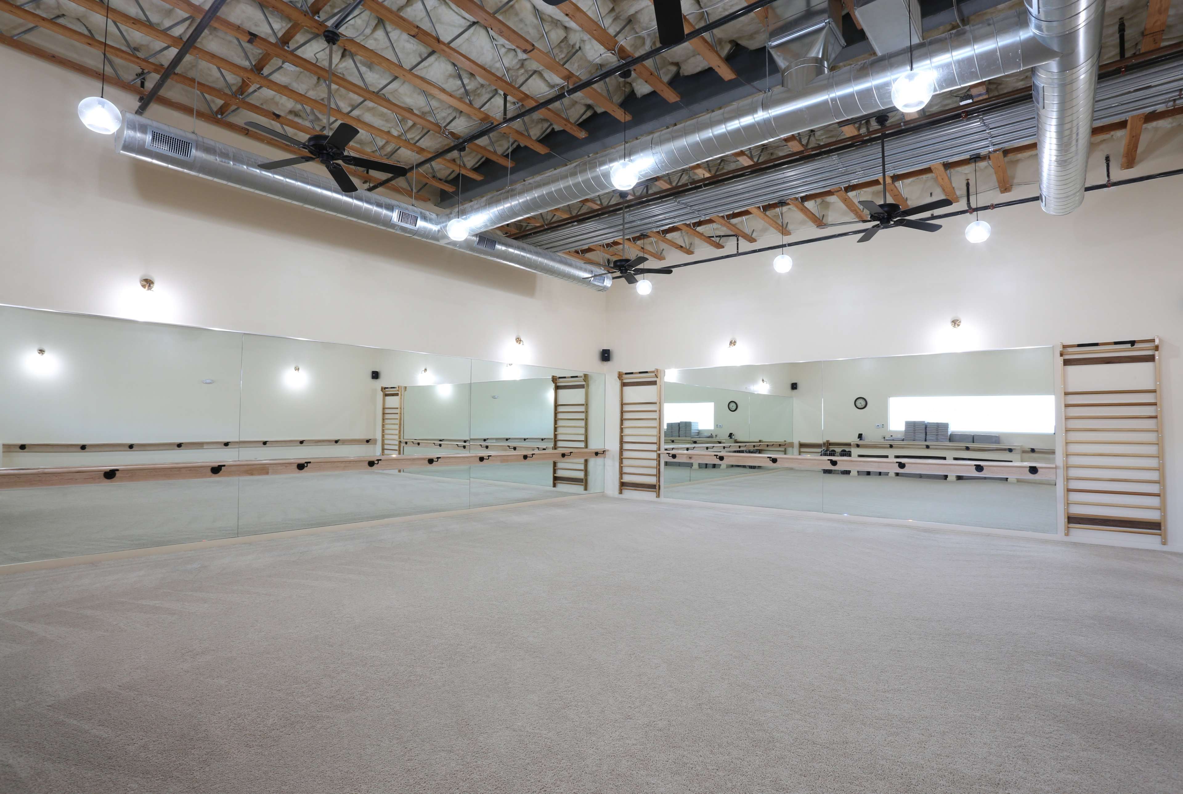 A spacious dance or exercise studio with mirrored walls, wooden beams, and a carpeted floor.