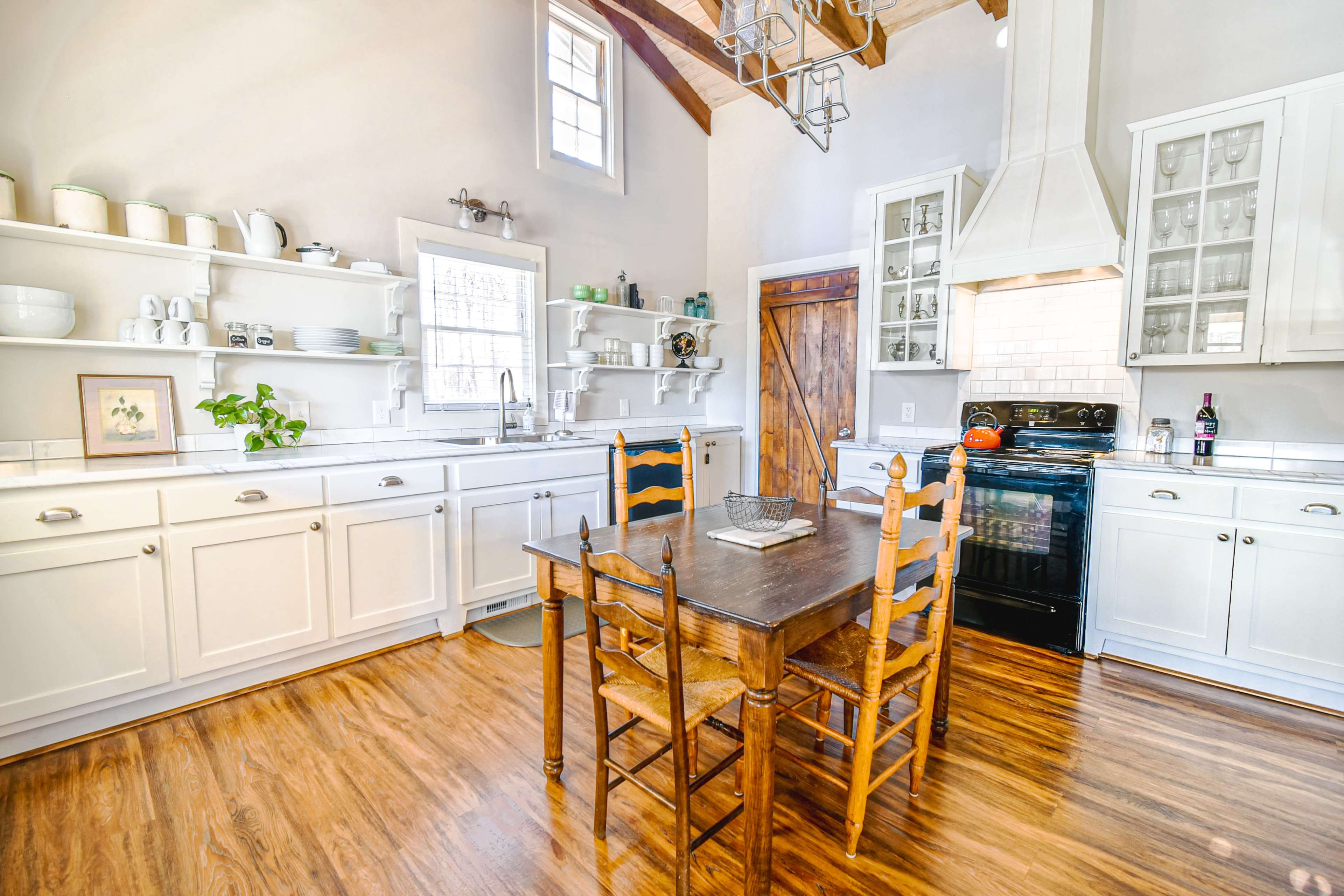 A kitchen features white cabinets, wooden flooring, a wooden table with chairs, and an oven against the wall.