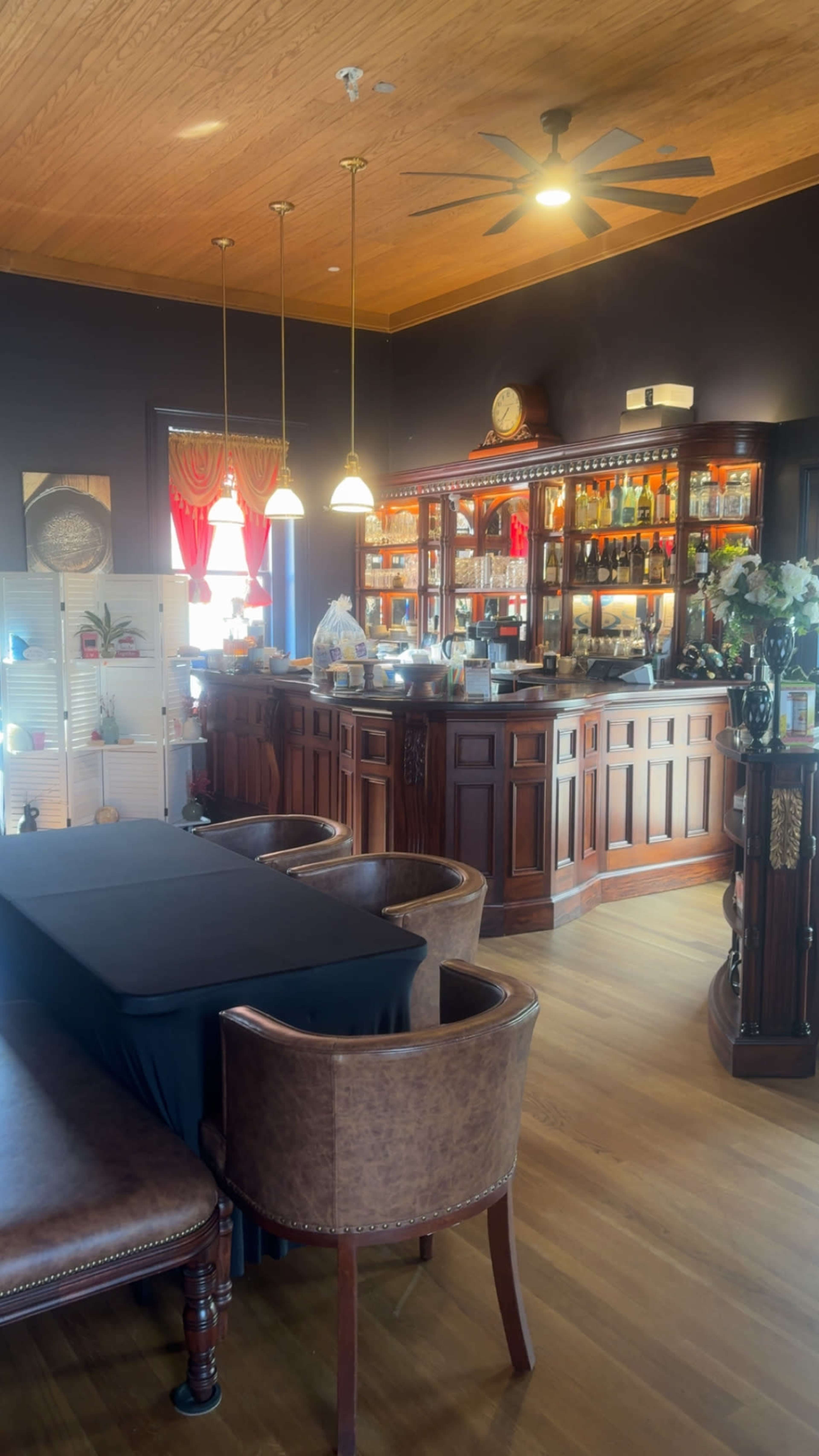 The image depicts the interior of a restaurant with a polished wooden bar, a black table with chairs, and warm lighting from decorative fixtures.