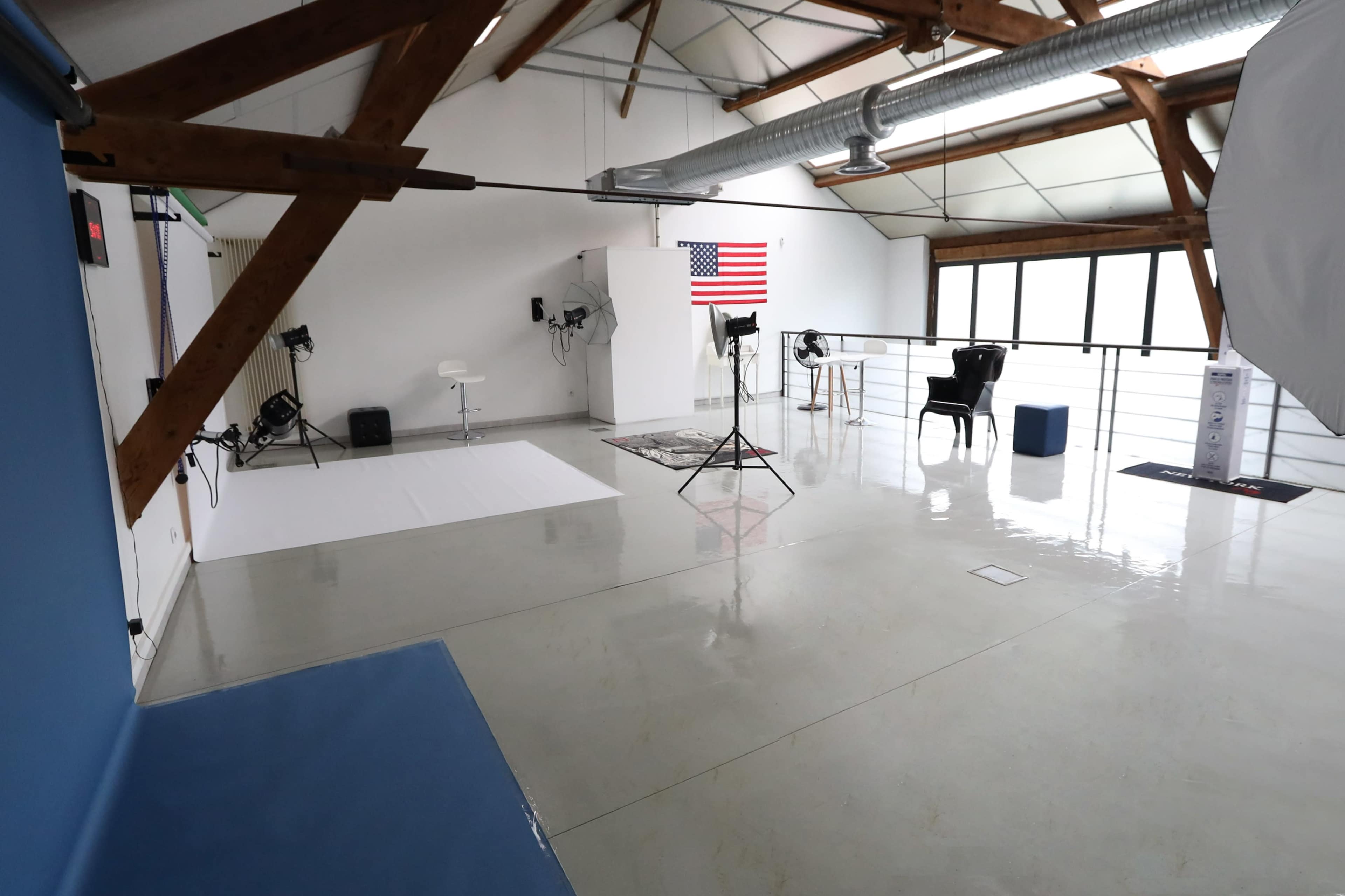 A spacious photography studio with wooden beams, a white backdrop, lighting equipment, and an American flag displayed on the wall.