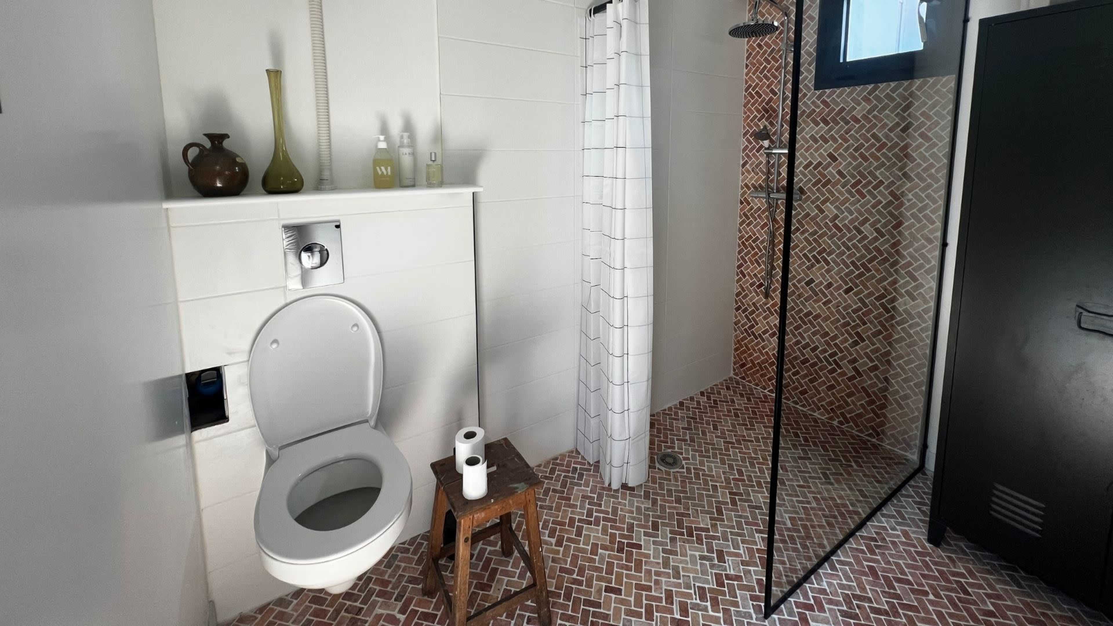 The image shows a modern bathroom featuring a toilet, a shower with glass doors, and patterned tile flooring.