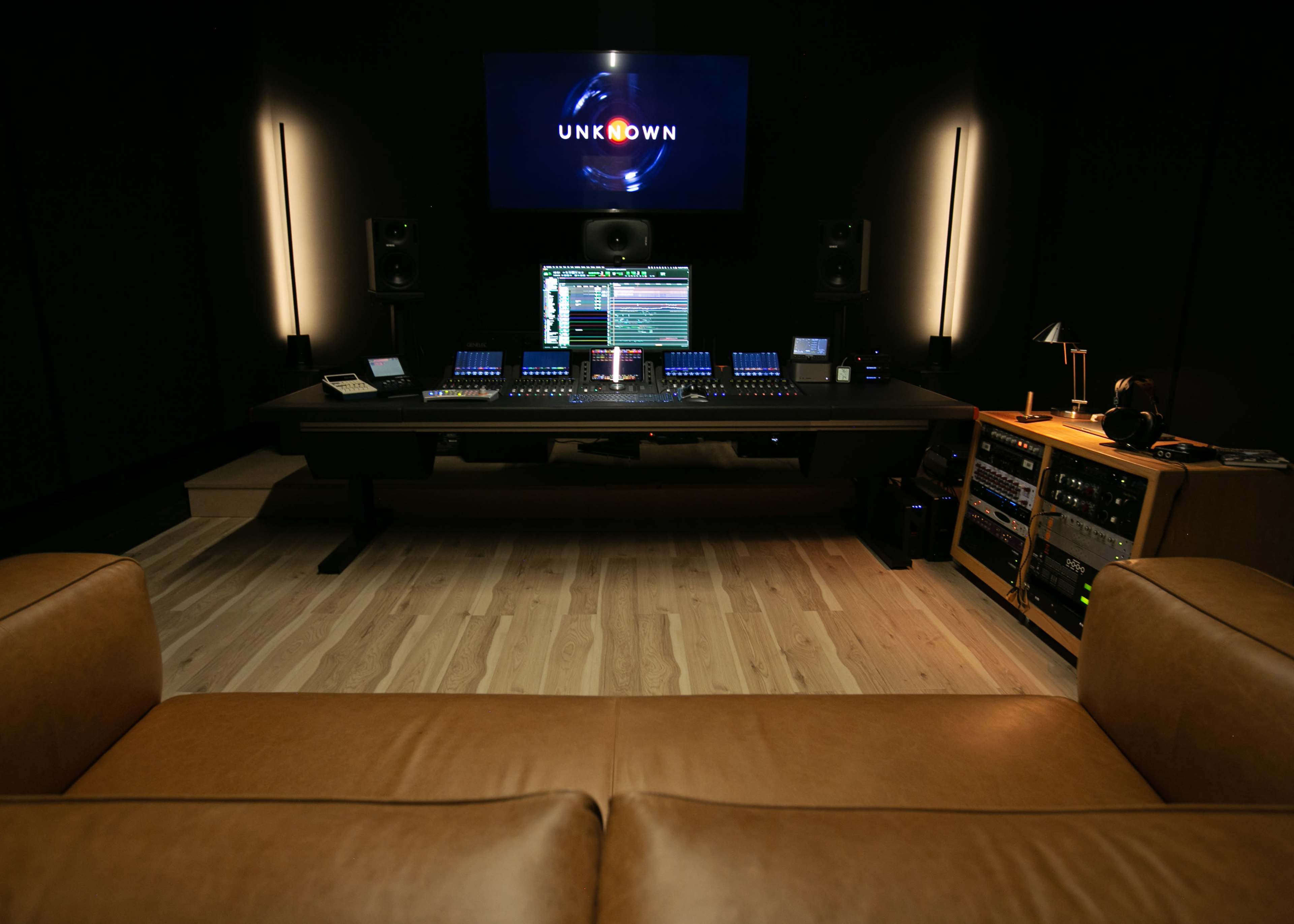 A modern audio production studio with a large mixing desk, sound equipment, and a display screen featuring the word "UNKNOWN."