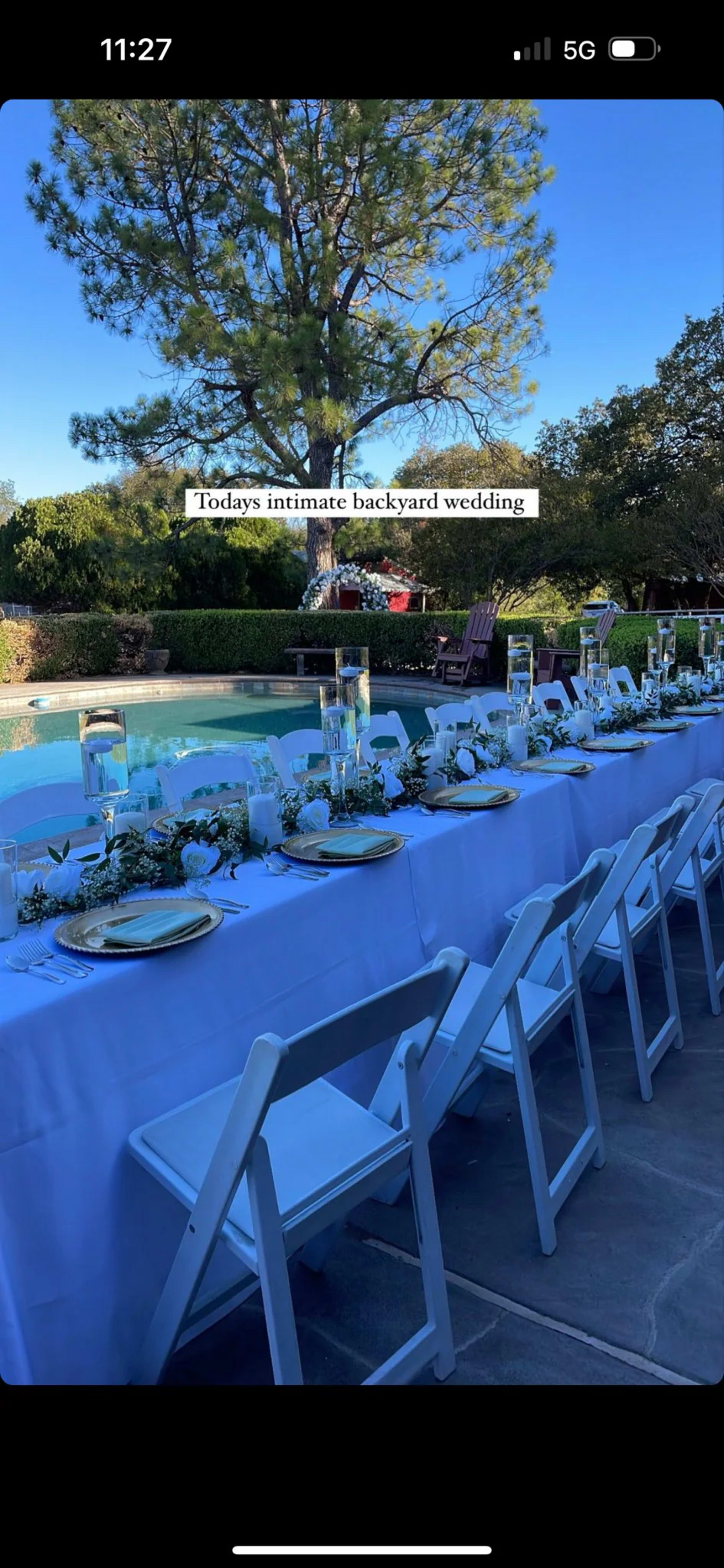 A long table set for an outdoor wedding by a pool, adorned with floral decorations and glass candle holders.