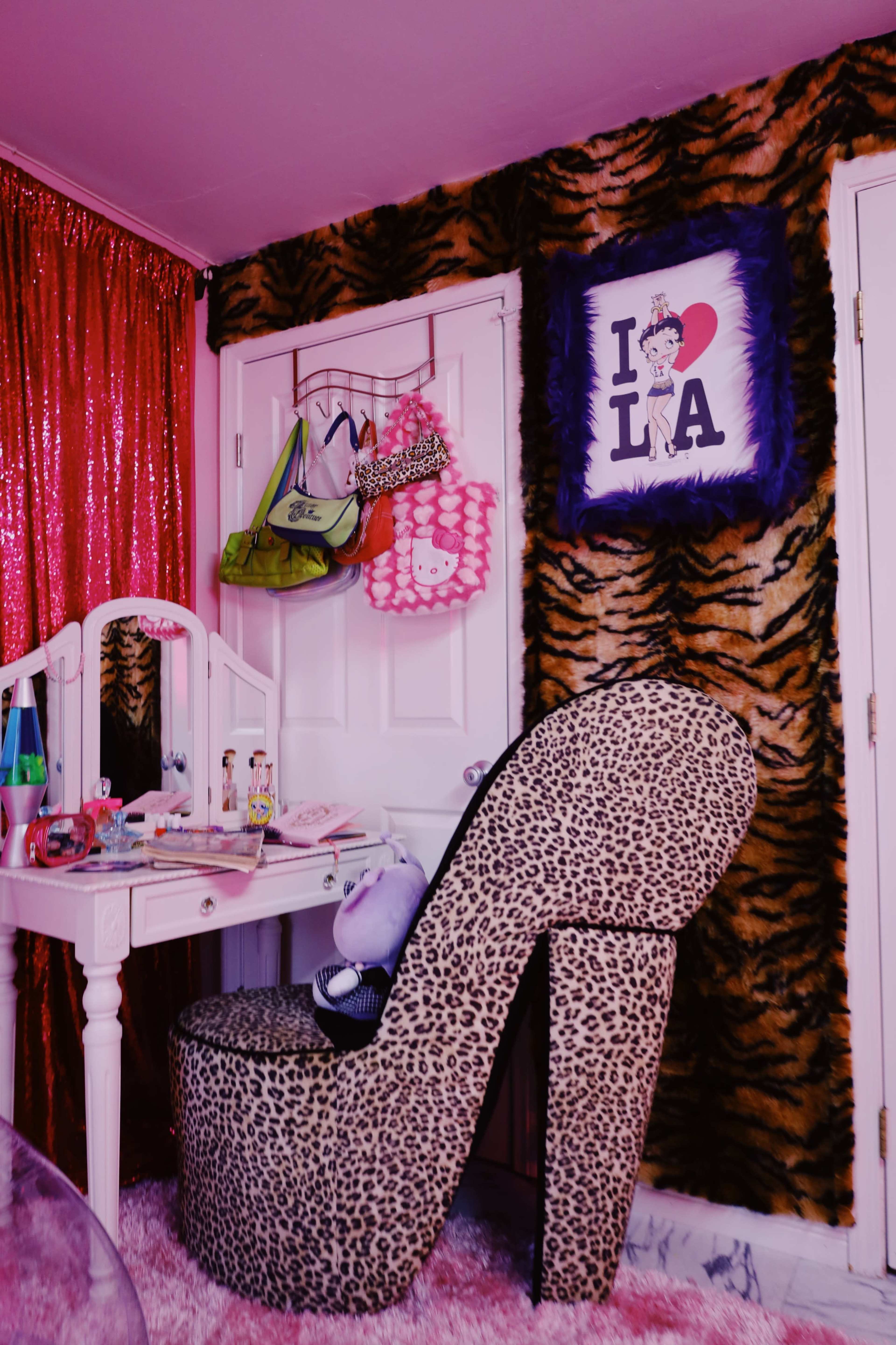 The image shows a vibrant room decorated with a large high-heeled chair, a vanity table, and colorful wall art featuring "I ♥ LA."