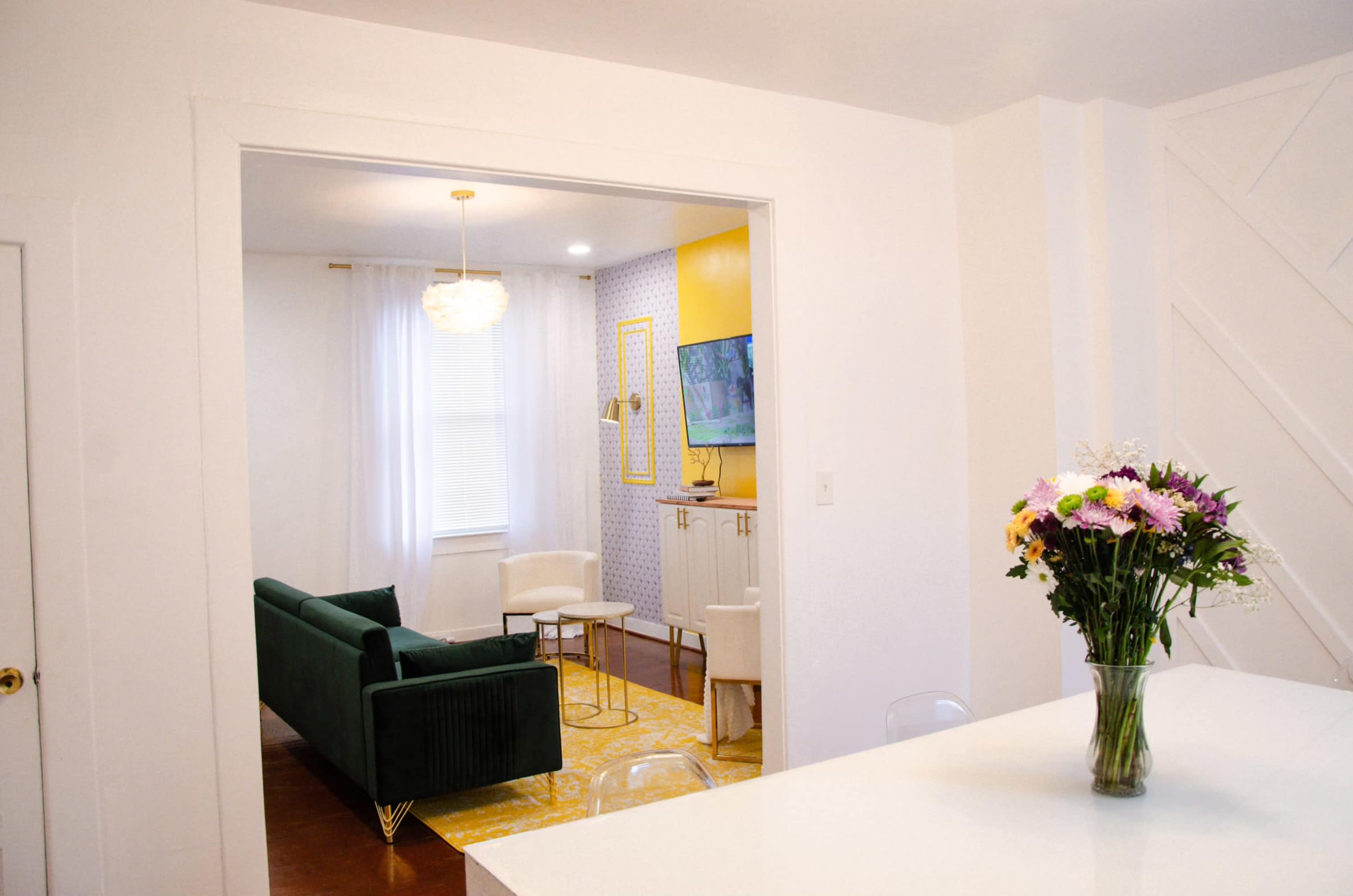 A bright interior space connects a dining area with a living room featuring a green sofa and a television.