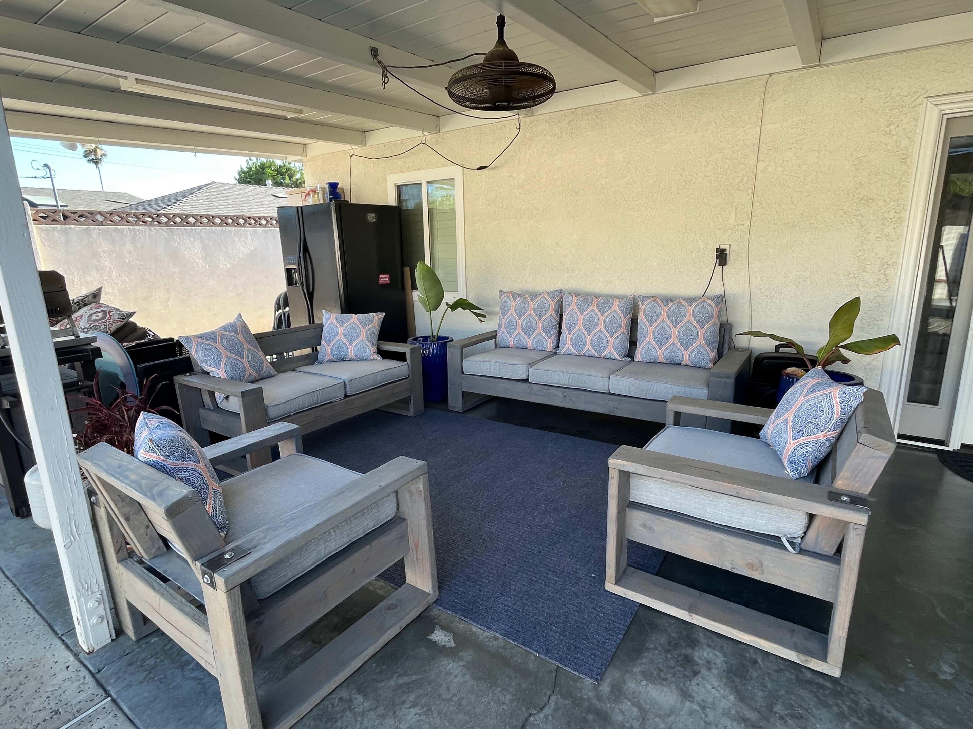 A patio with a set of gray outdoor sofas and chairs arranged around a blue rug under a covered area.