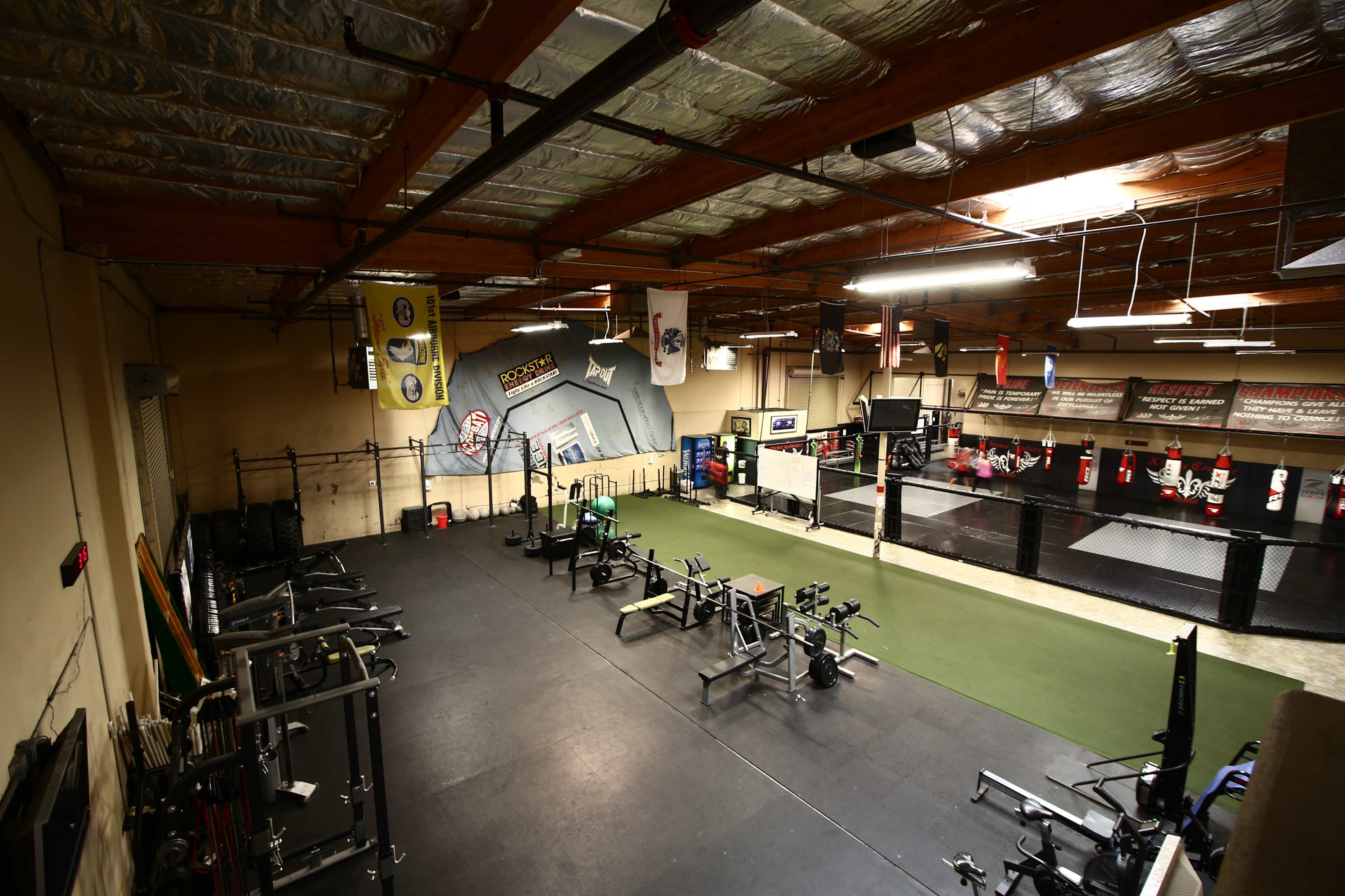 A spacious gym with various exercise equipment on one side and a martial arts training area with a ring on the other side.