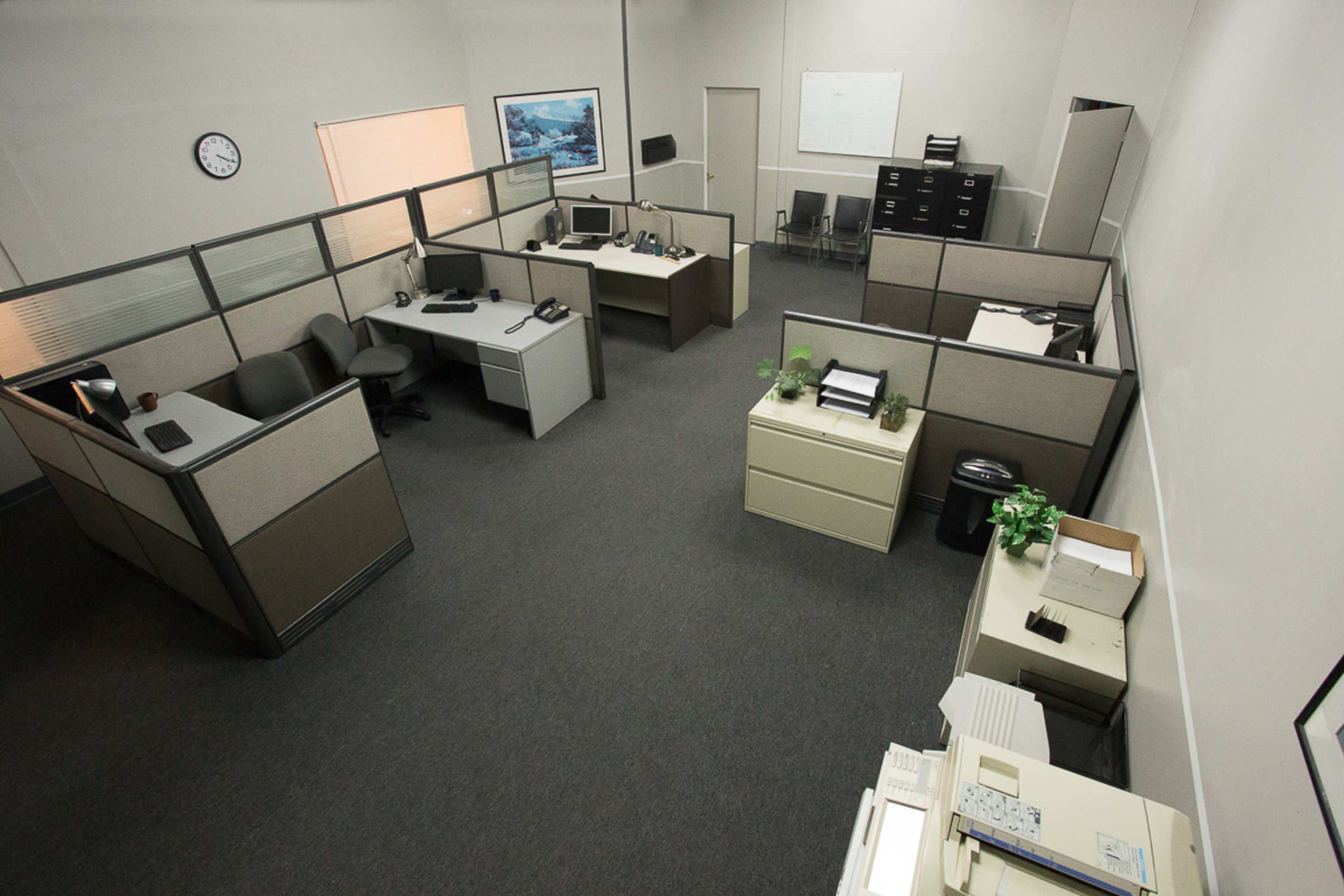 An organized office space with cubicles, desks equipped with computers, a filing cabinet, and a clock on the wall.