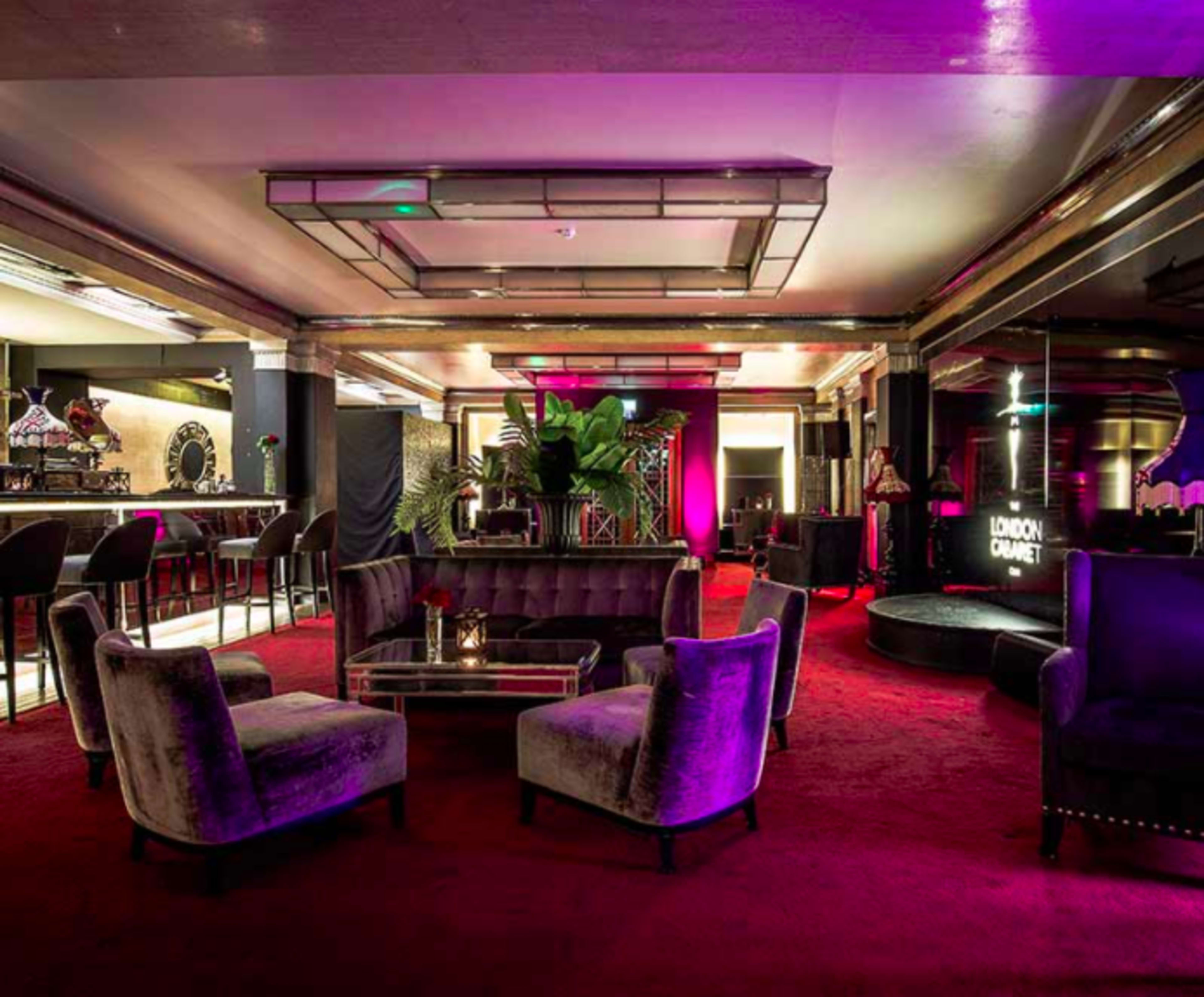 The interior of a lounge features plush seating with purple and pink lighting, a bar area, and elegant décor.