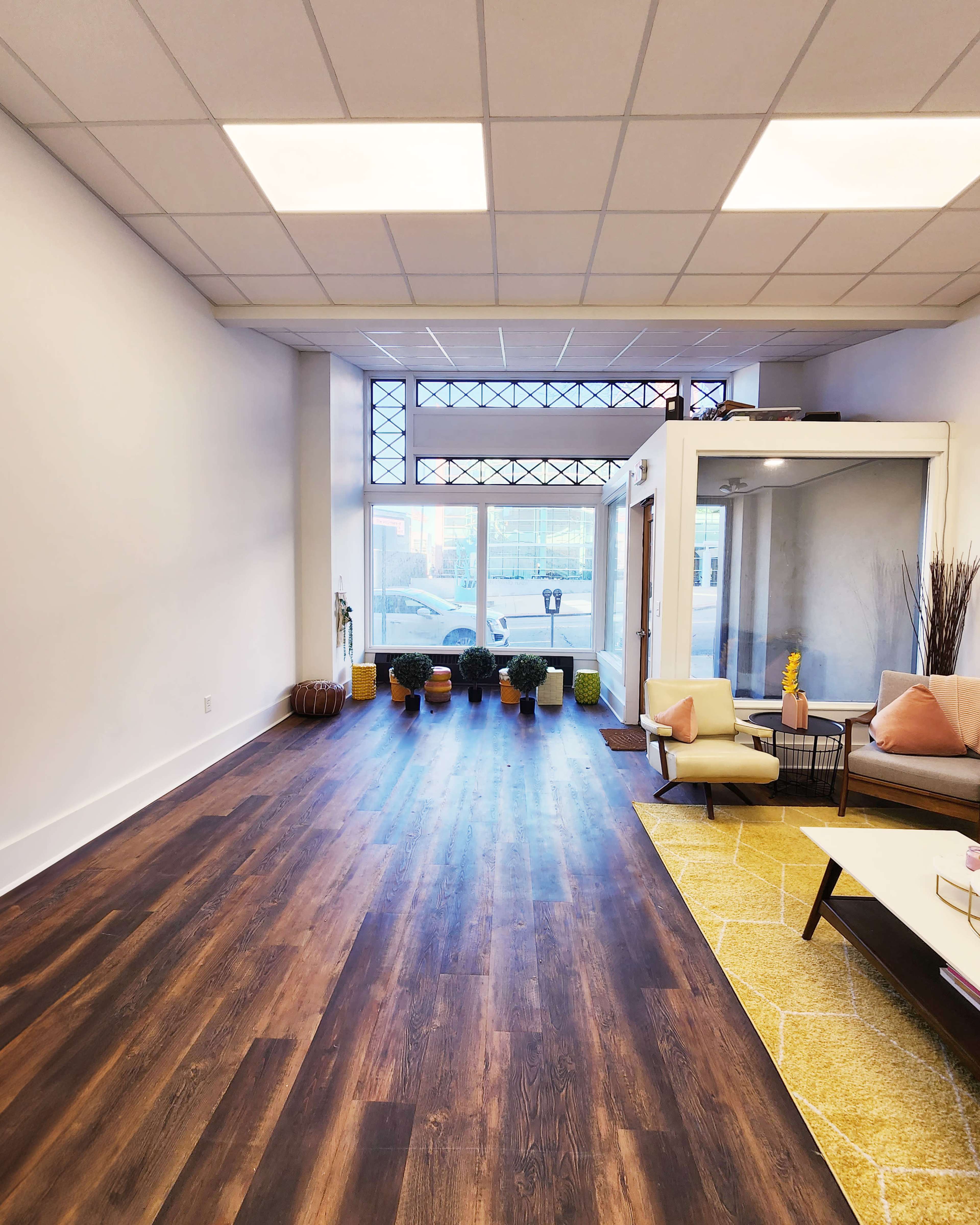 A modern, minimalistic interior of a waiting area featuring hardwood floors, potted plants, and a seating arrangement with a coffee table.